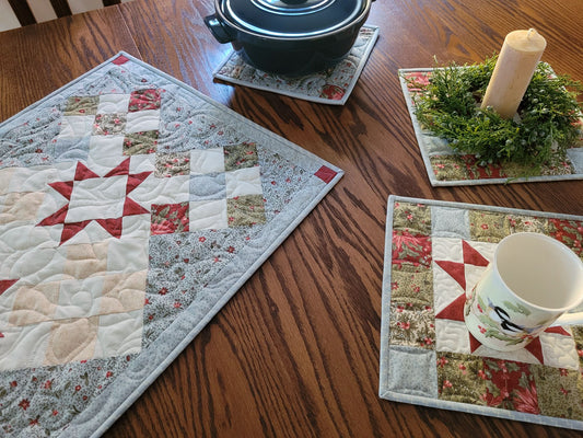 Quilts shown in lifestyle shot with Christmas greenery, candle and mug.