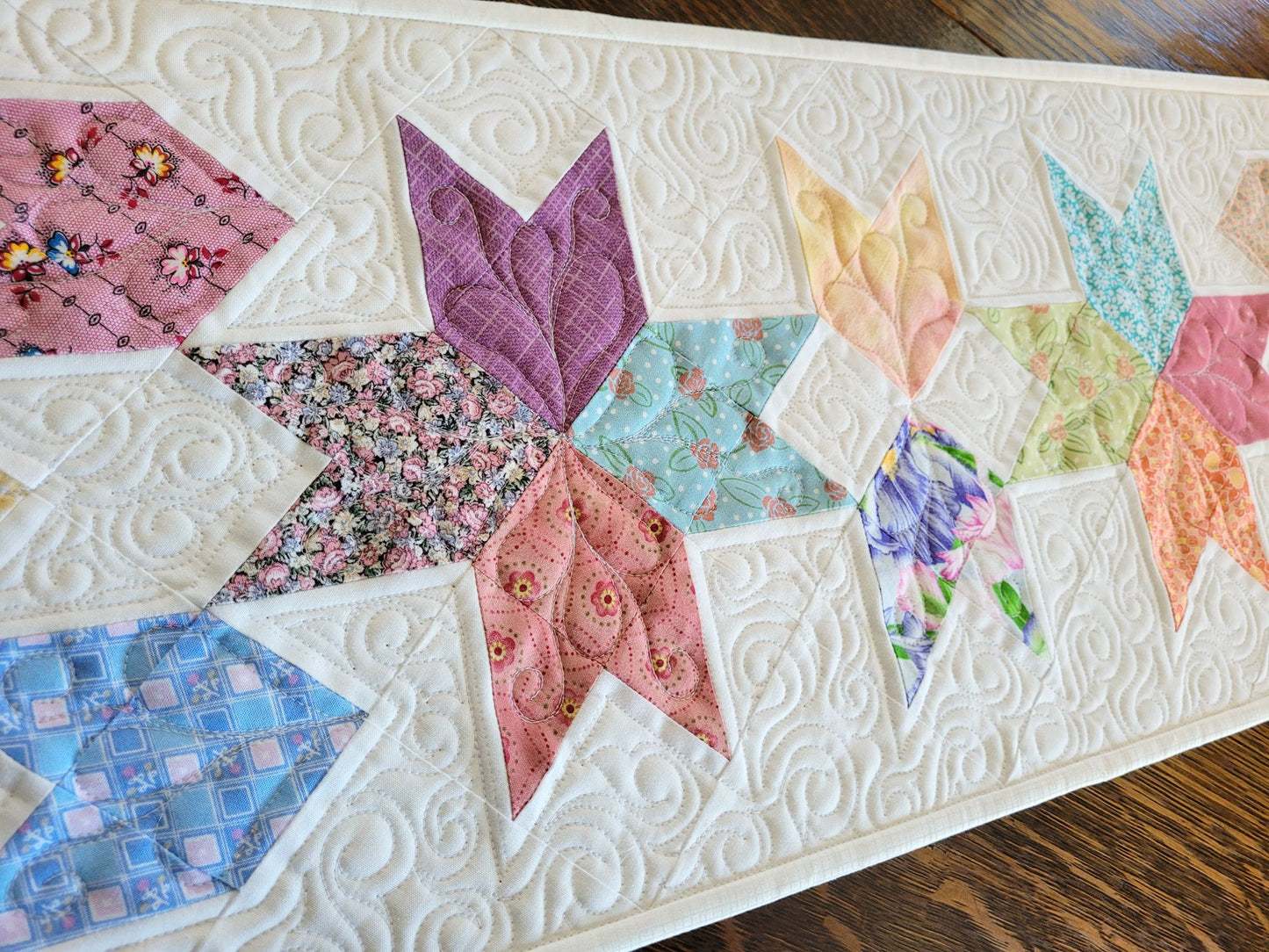 Spring tulip table runner in pastel patchwork on white background, shown in angled view to show quilting texture.