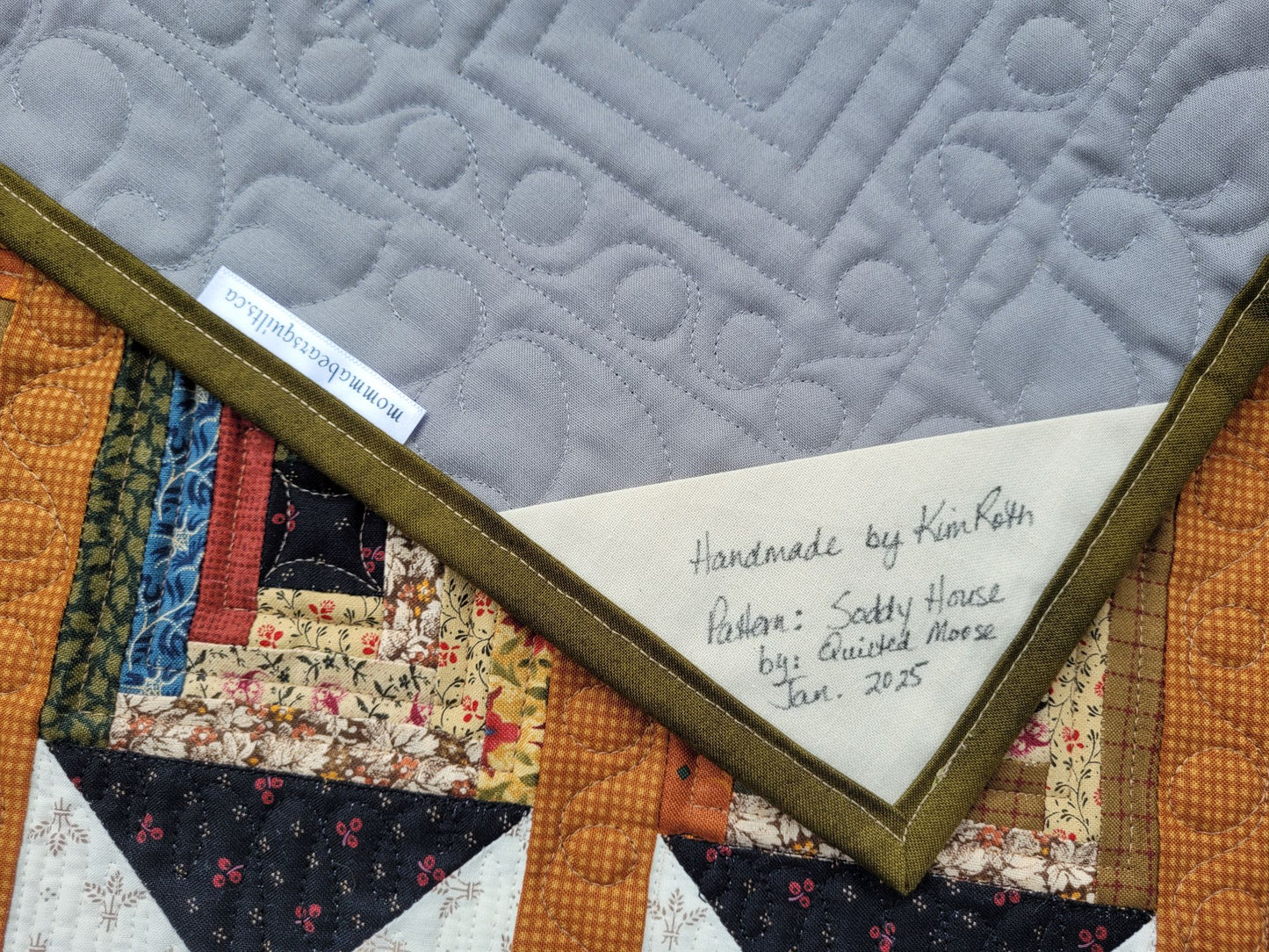 Quilt back with a label indicating 'handmade by Kim Roth' and date.