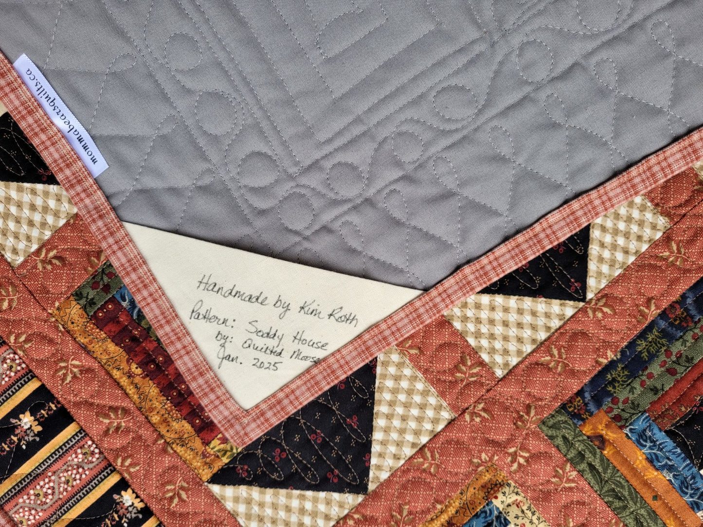 Quilt with a label indicating 'Handmade by Kim Roth' on a gray background