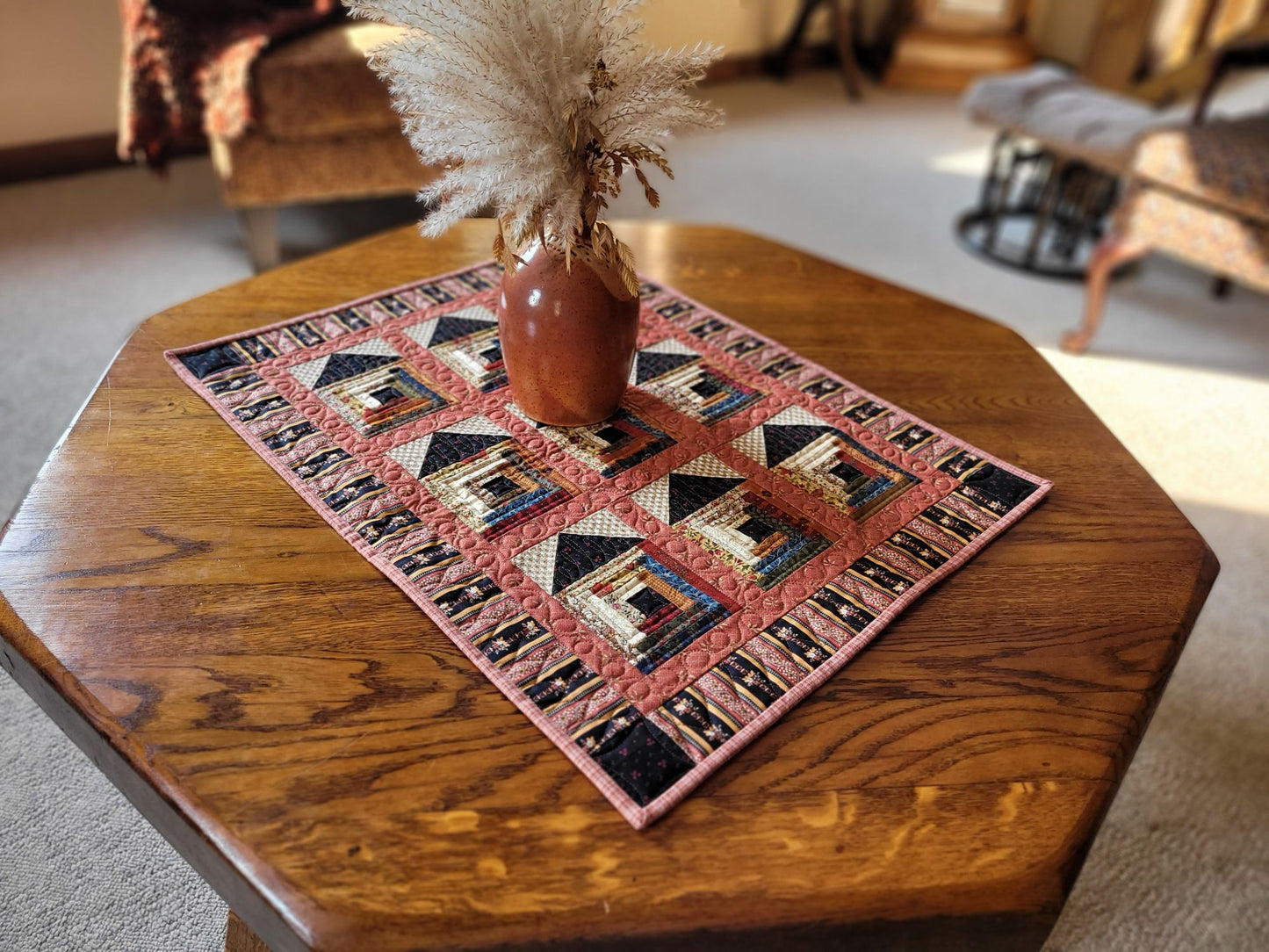 Quilted table runner with log cabin house pattern on a wooden table in living room setting