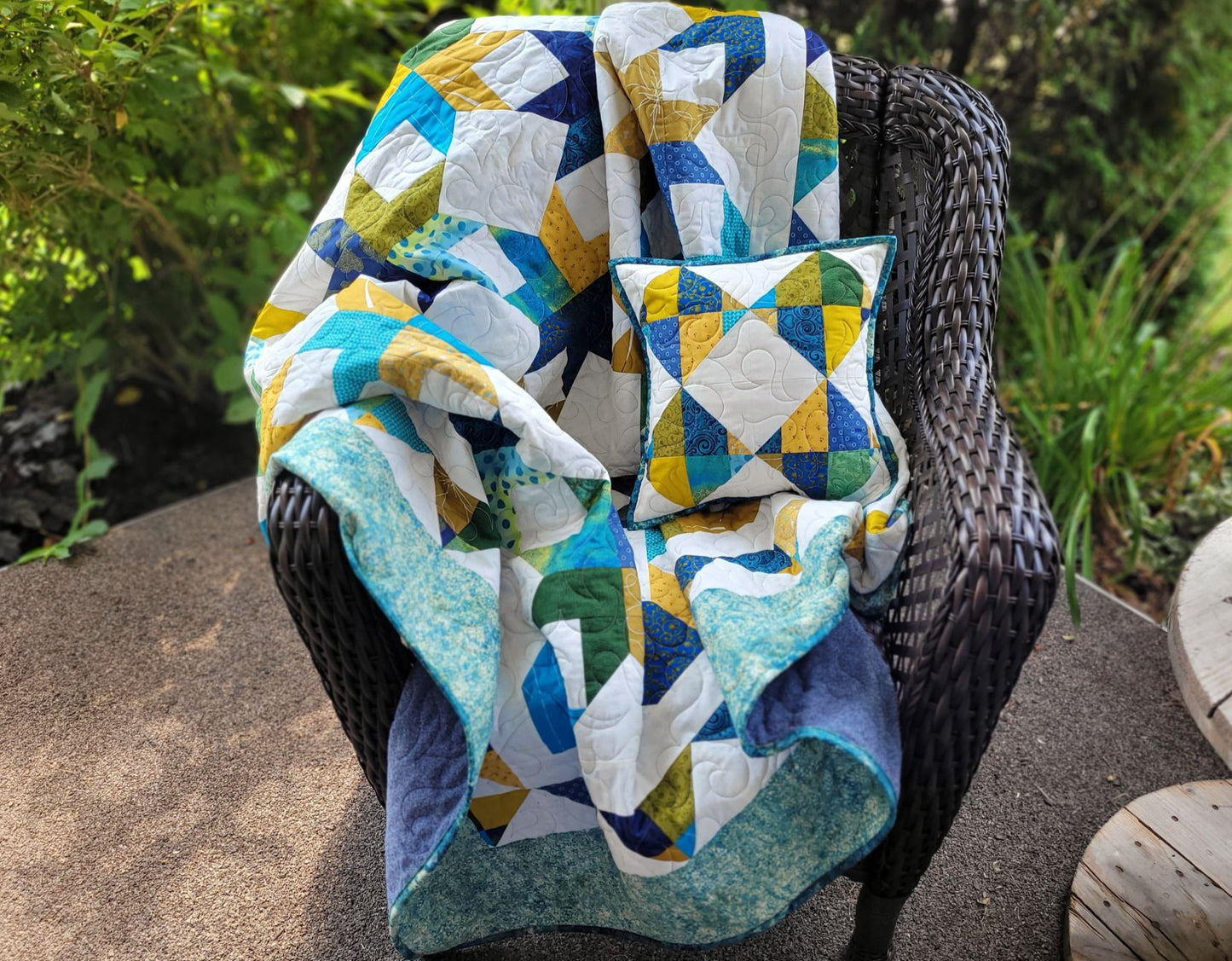 Throw quilt and matching pillow shown outdoors on a brown wicker chair.