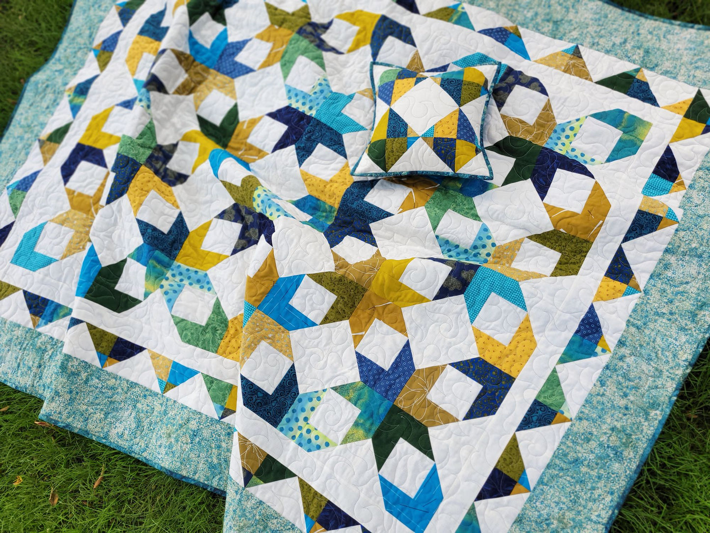 Scrappy star throw quilt and matching pillow is shown outdoors on grass.