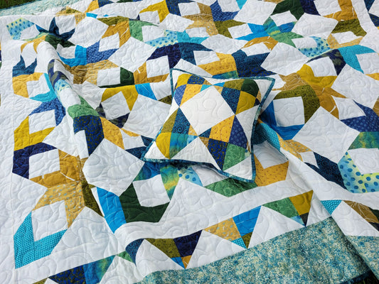 Quilted throw with matching pillow done in scrappy star pattern in tones of blue, gold and green on white background.