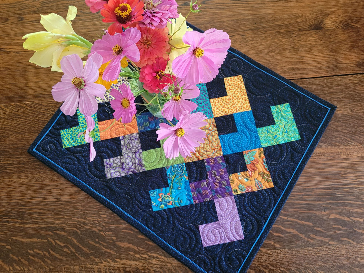 Colorful quilted table mat with a vase of flowers on a wooden surface