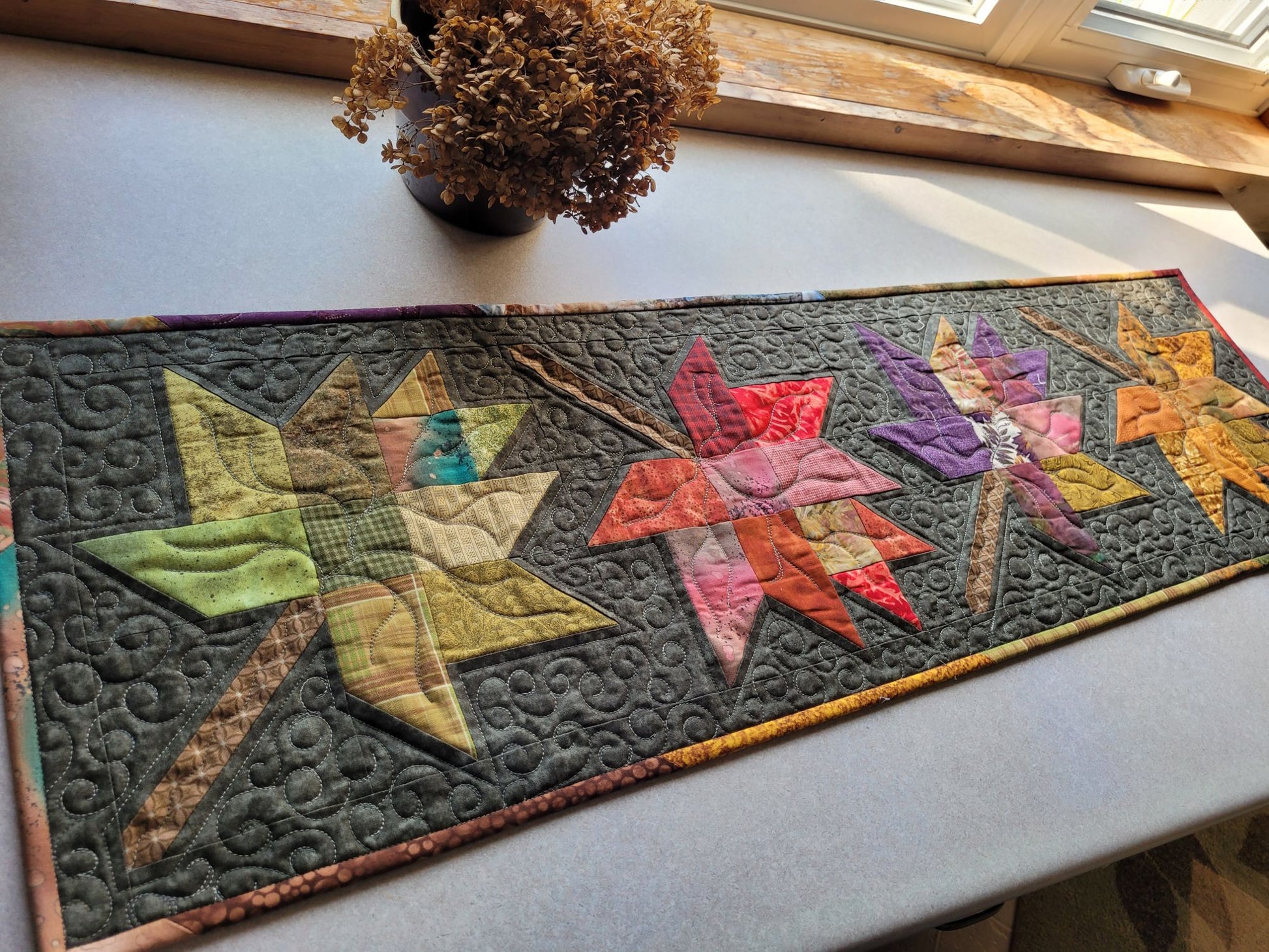 Quilted table runner with colorful leaf patterns on a light surface.