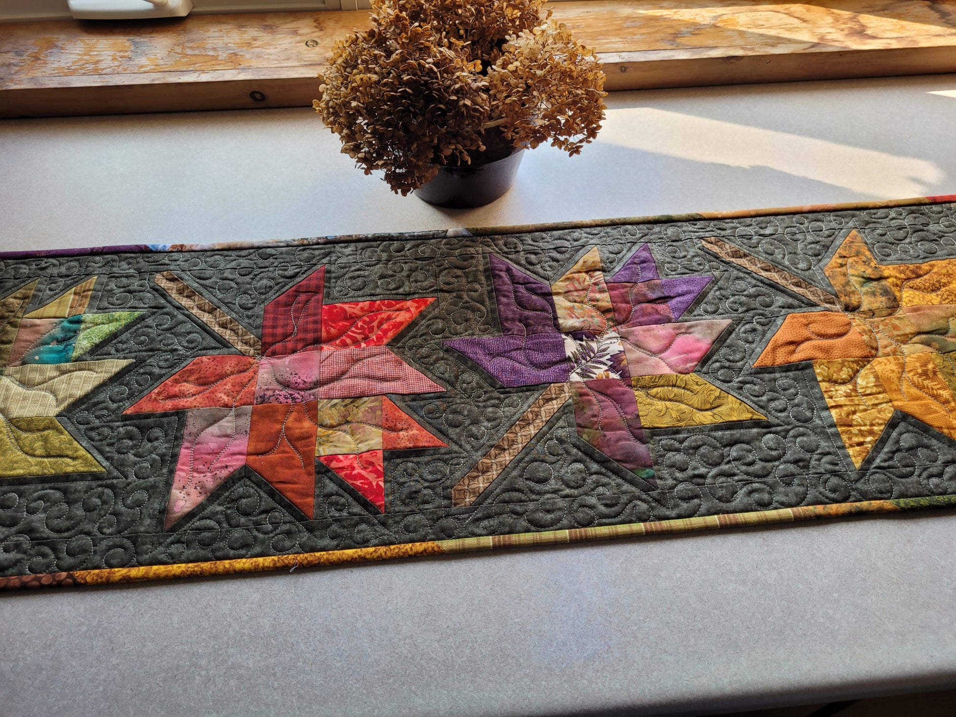 Colourful leaf-patterned quilted table runner on a countertop with a plant in the background