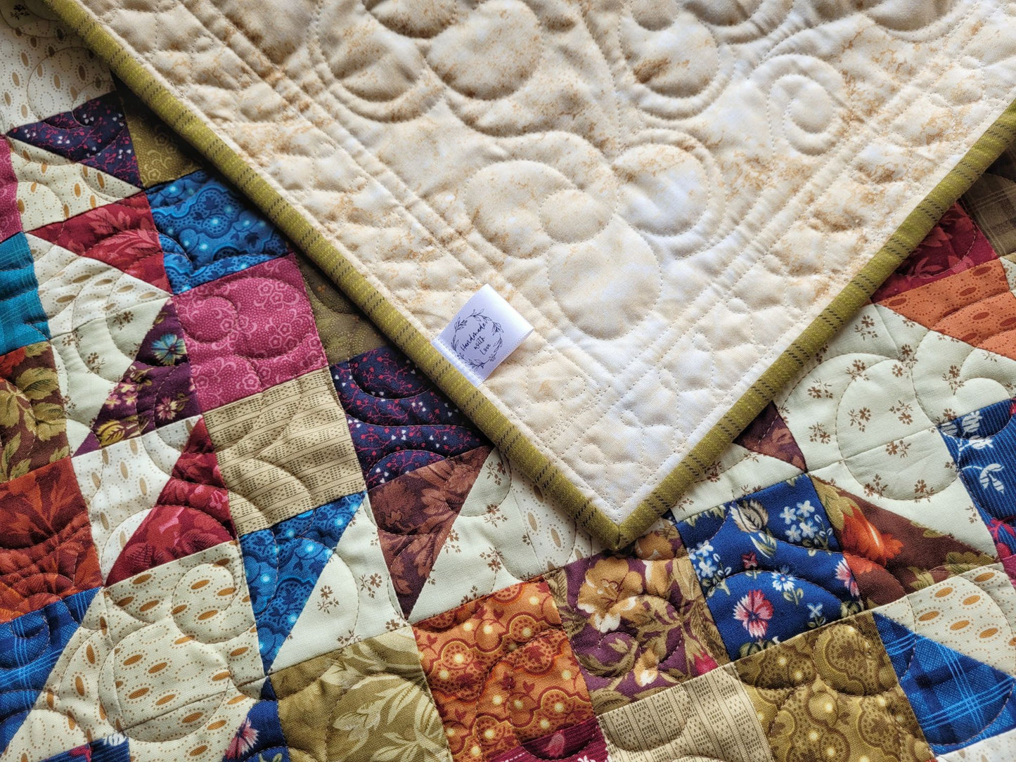 Quilt with colourful patchwork design, with the corner folded over to show backing and handmade label.