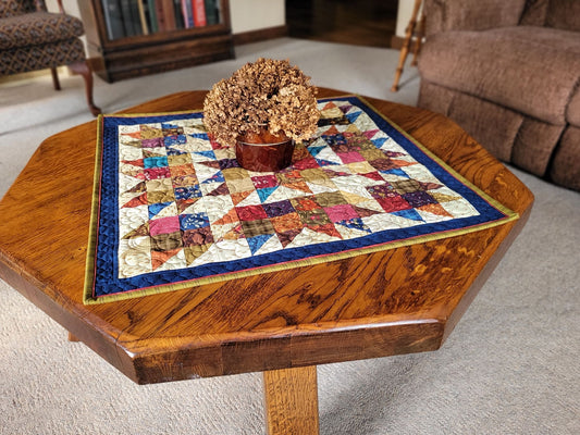 Wooden coffee table with a colorful quilted tablecloth and decorative pot in a living room setting.