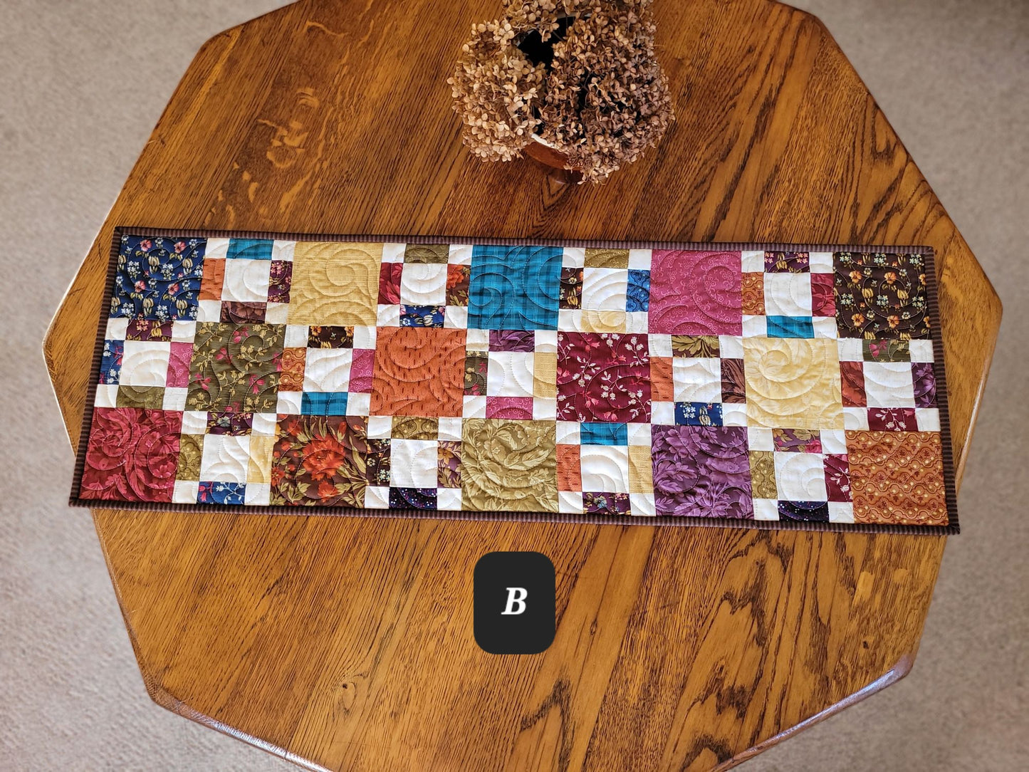 Colourful patchwork table runner on a wooden table with a label B.
