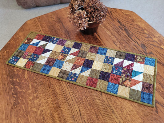 Quilted table runner on a wooden table with a small pot of dried flowers.