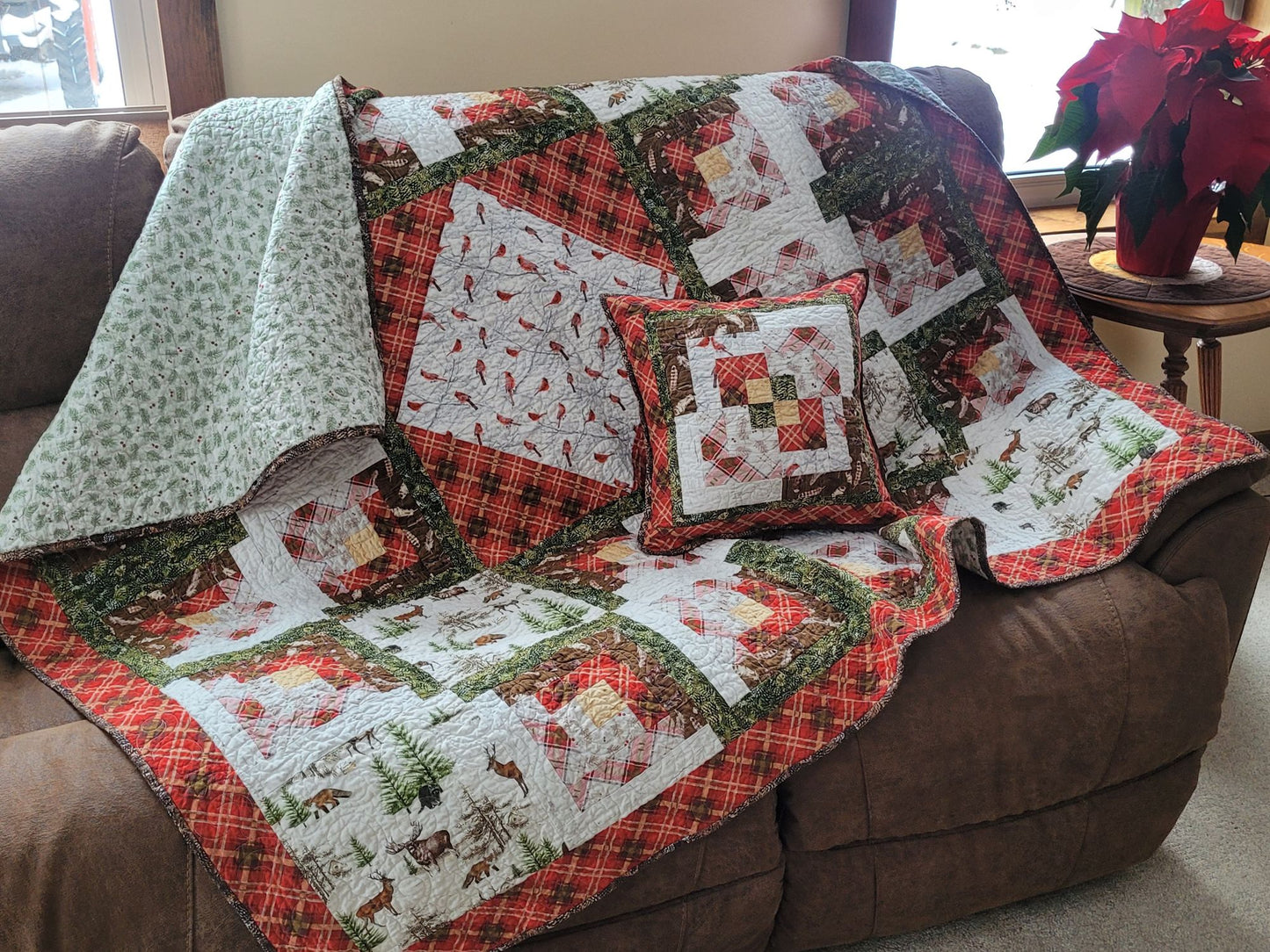 Quilt with winter woodland patterns draped over a brown sofa in a living room.