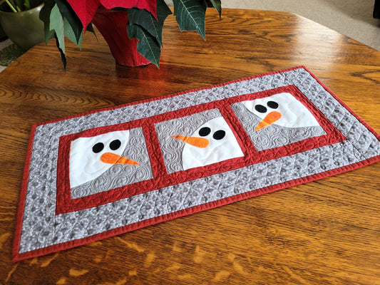 Quilted table runner with snowman design on a wooden table