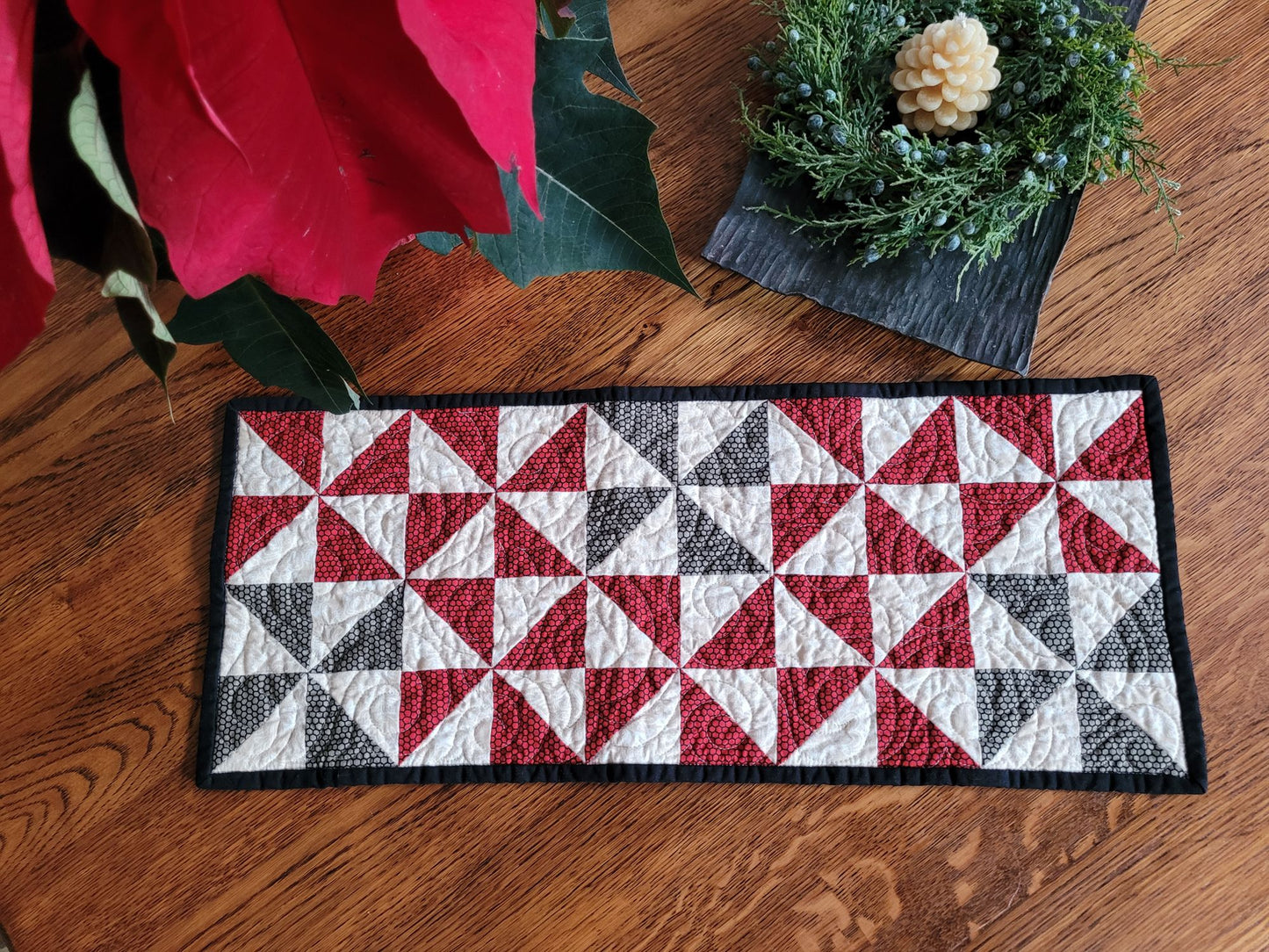 Quilted runner with red, white, and black pattern on a wooden surface
