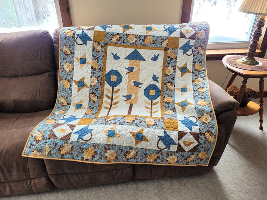 Thoughts of Spring throw quilt features applique blue birds, birdhouse, stars, flowers, baskets and lovely coordinating floral fabrics in blue brown, gold and yellow.
