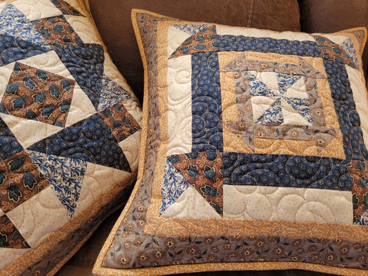 Close up of two quilted patchwork pillows on a brown couch.