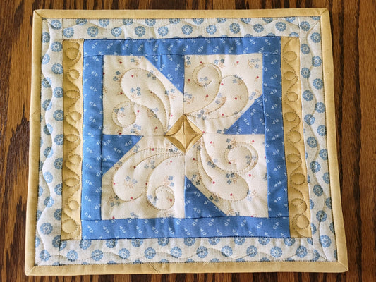 Quilted hot mat in blue and beige fabrics, with a patchwork flower.