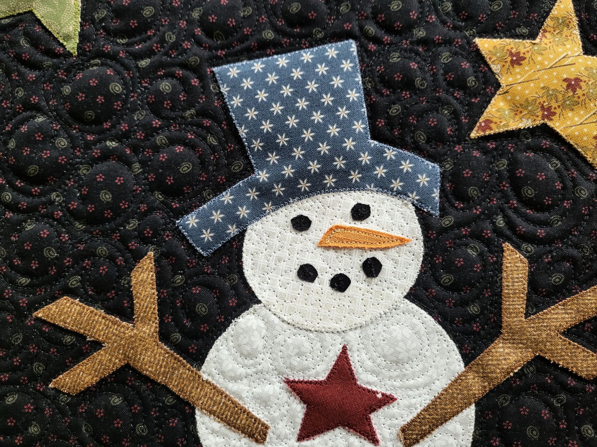 Showing close up snowman detail with blue hat, carrot nose, coal eyes and mouth, red star button and stick arms. All shapes made from hand cut applique.