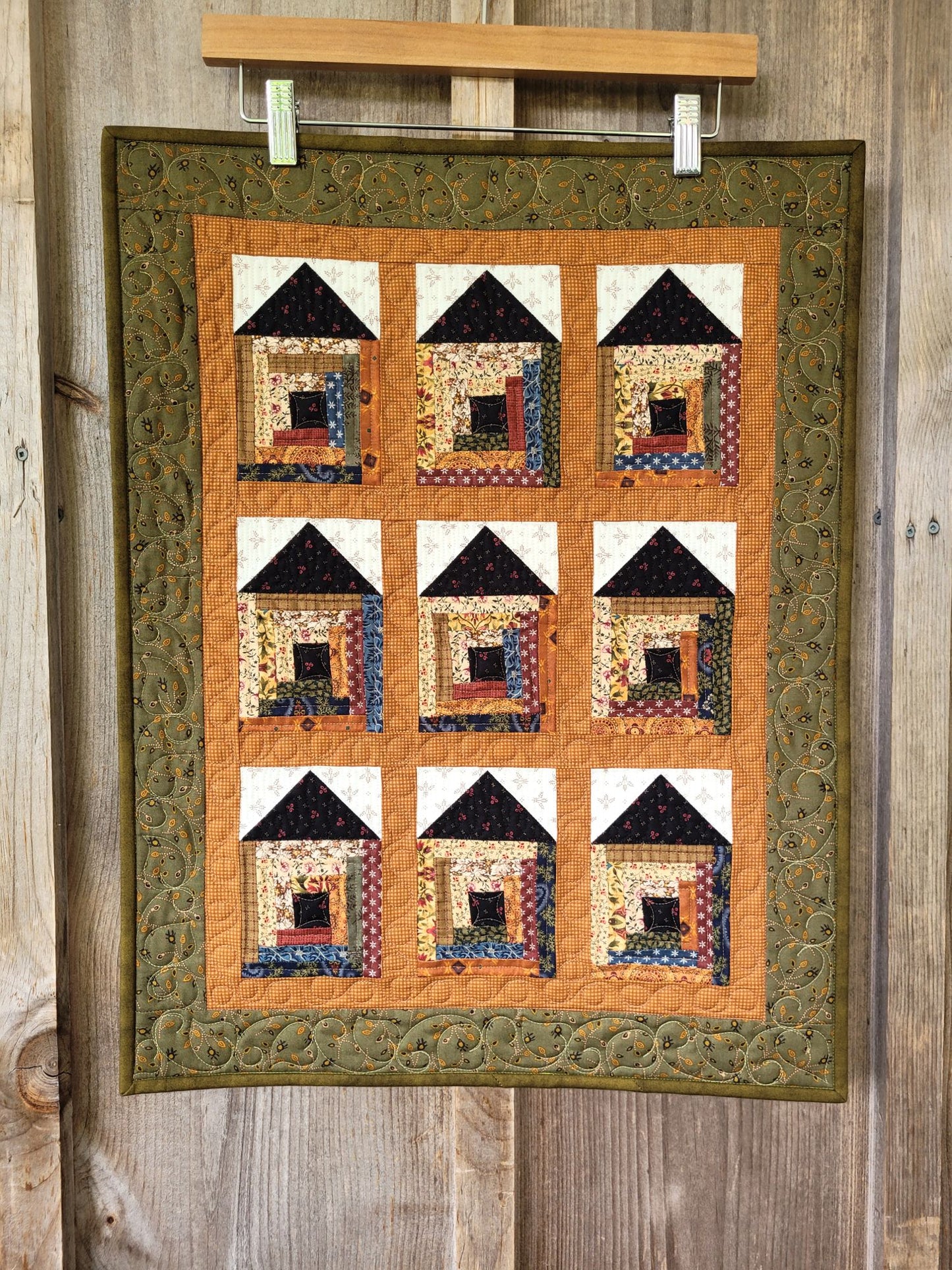 Quilt with house pattern hanging on a wooden wall