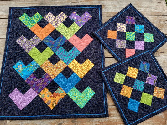 Bright Table Topper with Patchwork Hearts and two matching mini quilts on wooden surface.