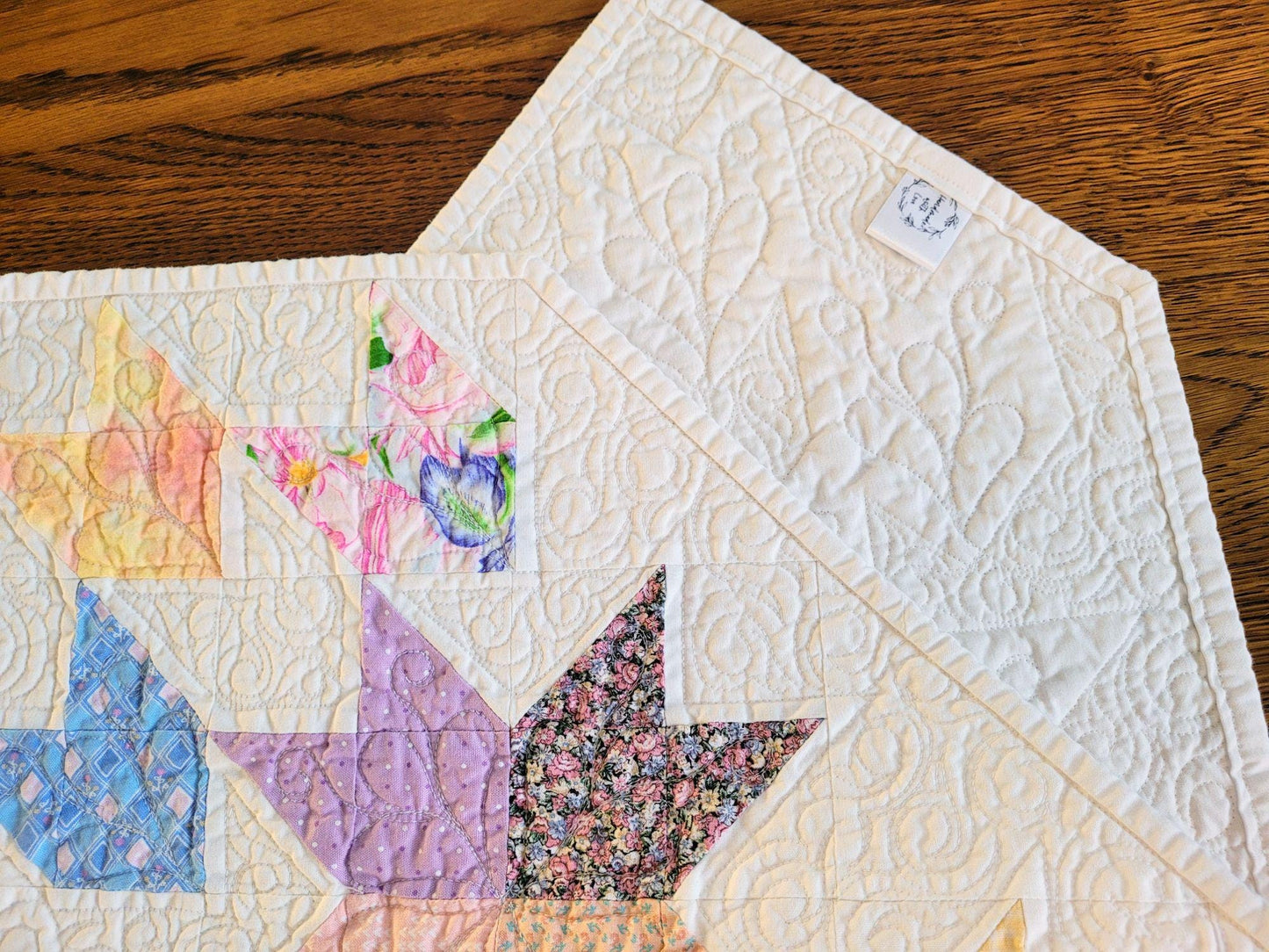 Close up of a folded quilted table runner showing the back with a handmade label, on a wood surface.