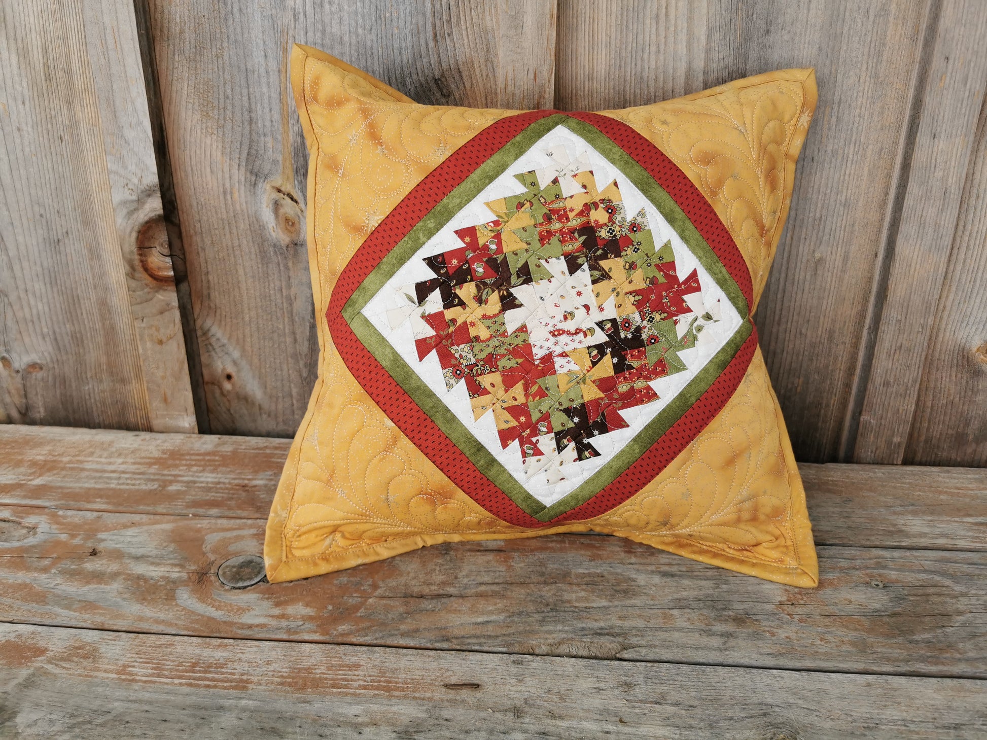 This patchwork pillow features intricate little twisters, in a wreath shape, in the center area. Framed by borders in green, red and gold that mirror the twisters makes for a eye catching, coordinating cushion.