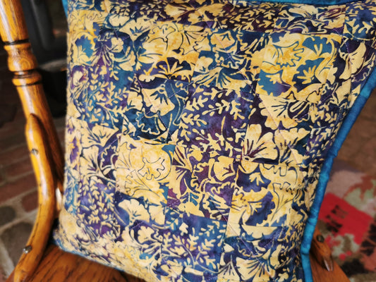 blue, purple and beige batik fabrics make up the front of theis throw pillow. Simple patchwork squares of coordinating fabrics make a subtle pattern.