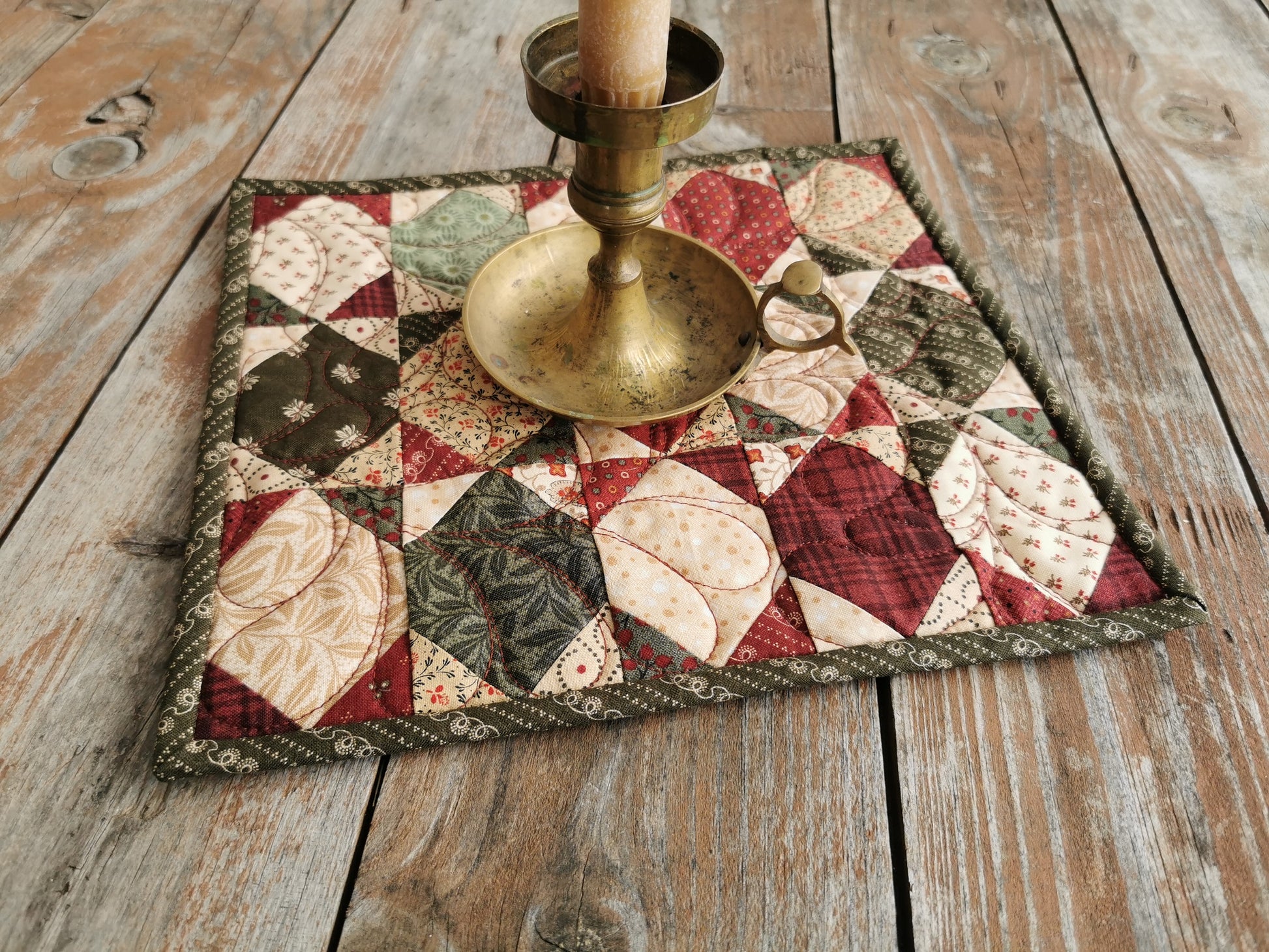 lifestyle shhot of red and green mini quilt with brass candle stick