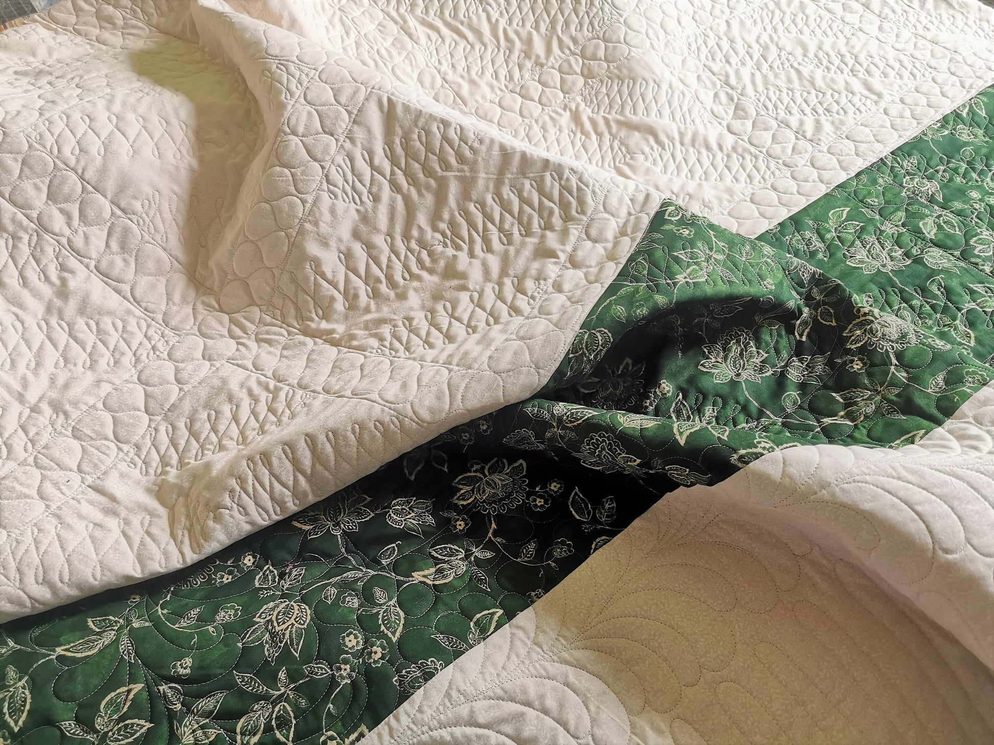 This shows the back of the vintage bed quilt. the backing is a tone on tone ecru print with a dark green stripe pieced across the one end. Stitching detail is easily seen on the back. 