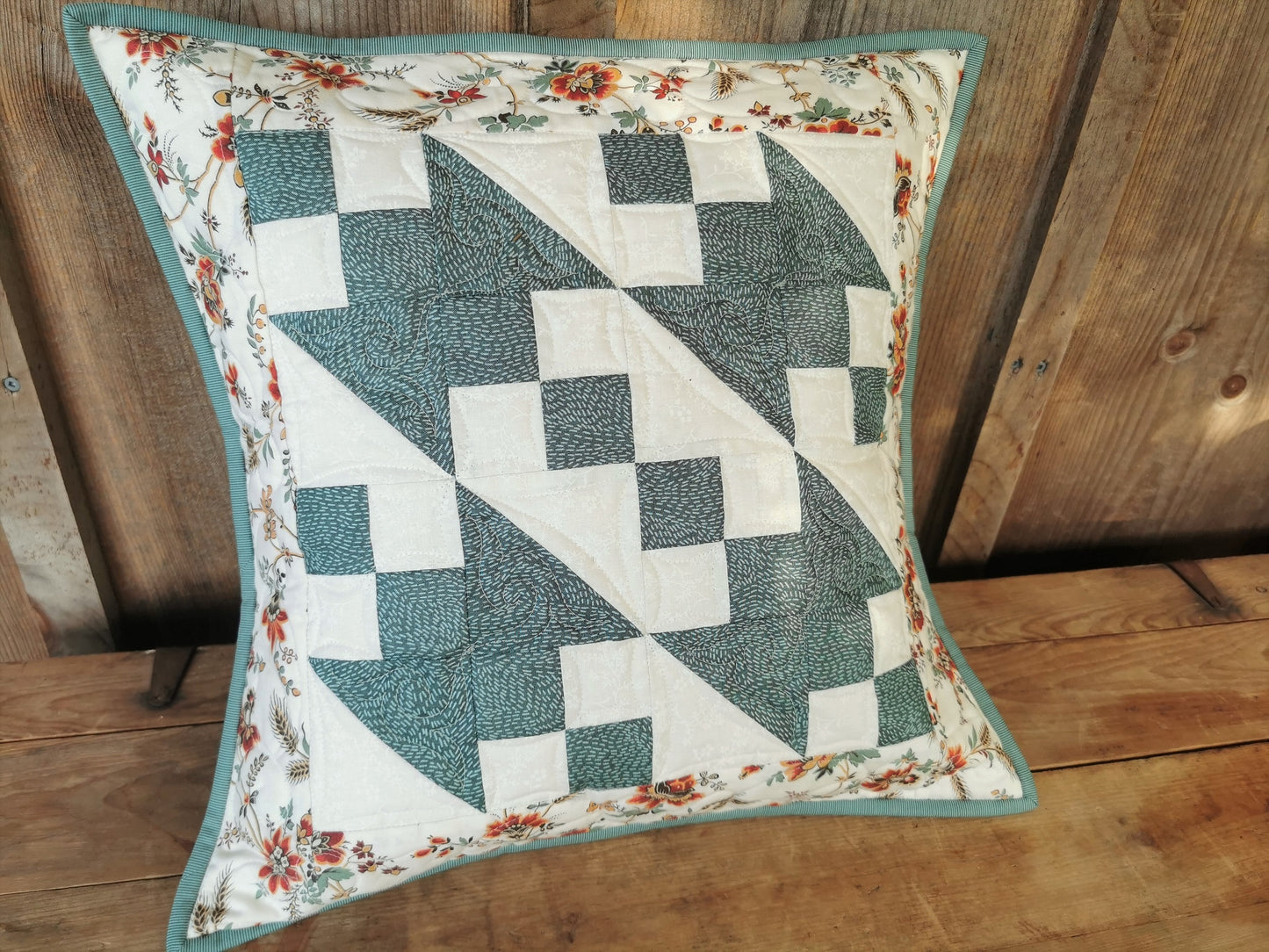 This striking patchwork pillow features teal and white piecing with a complimentary floral border.