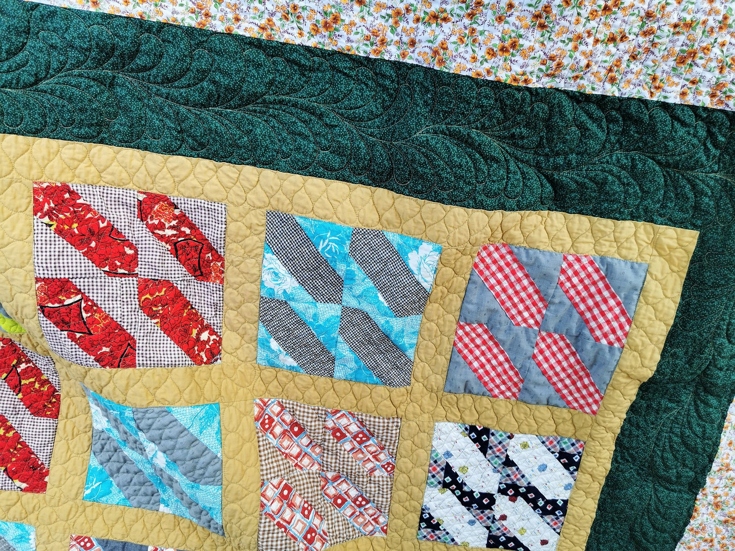 the vingage bed quilt is shown here with the dark green border prominent. I quilted freehand feathers on this border. You can see a bit of the floral outer border too. This has brown and burnt oragne flowers with green leaves on an ecru background. Also shown are more of the vintage patchwork blocks: brown gingham with a red slash, bright blue with gray gingham slash, gray with a red gingham slash, navy plaid with white slash. . 