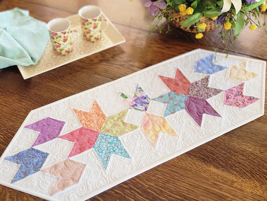 Spring tulip table runner in pastel patchwork on white background. Shown on table with a flower arrangement and mugs on a tray. 