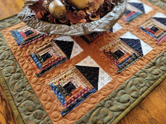 Quilted table runner with rustic log cabin house pattern on a wooden surface
