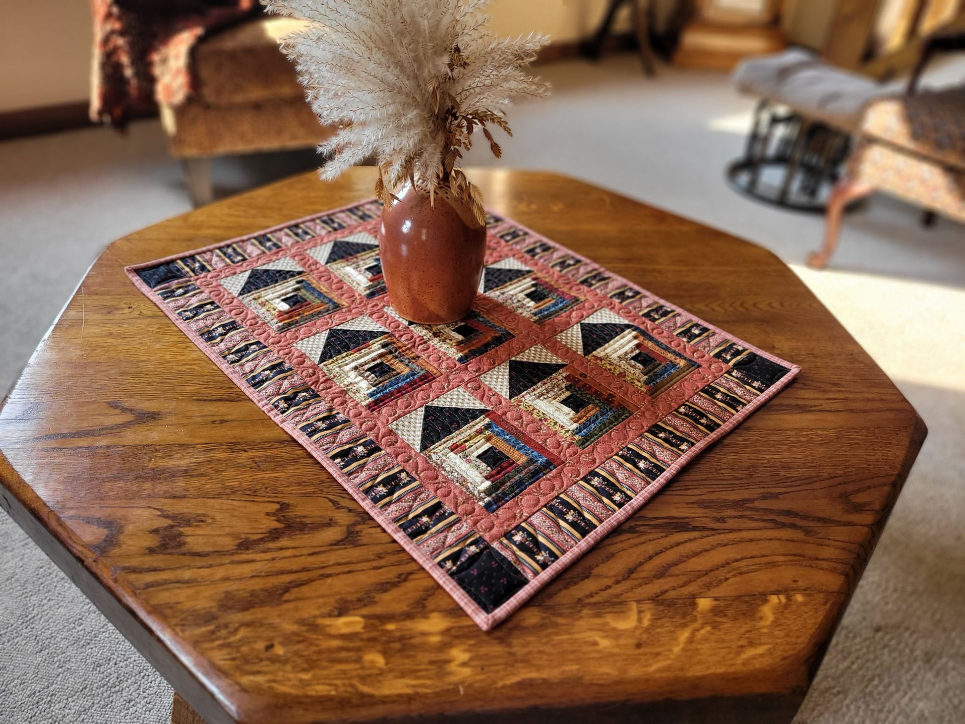 Quilted table runner with log cabin house pattern on a wooden table in living room setting