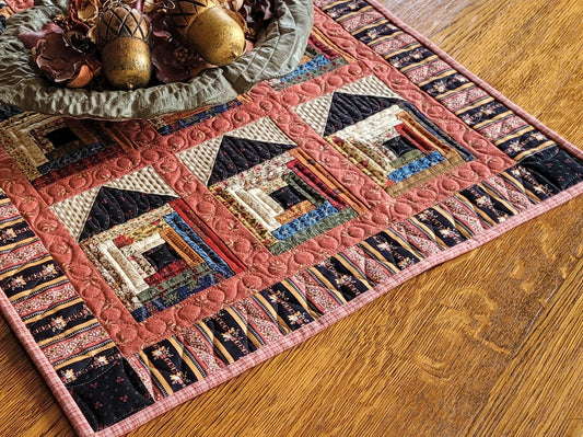 Quilted table runner with log cabin house pattern on a wooden surface
