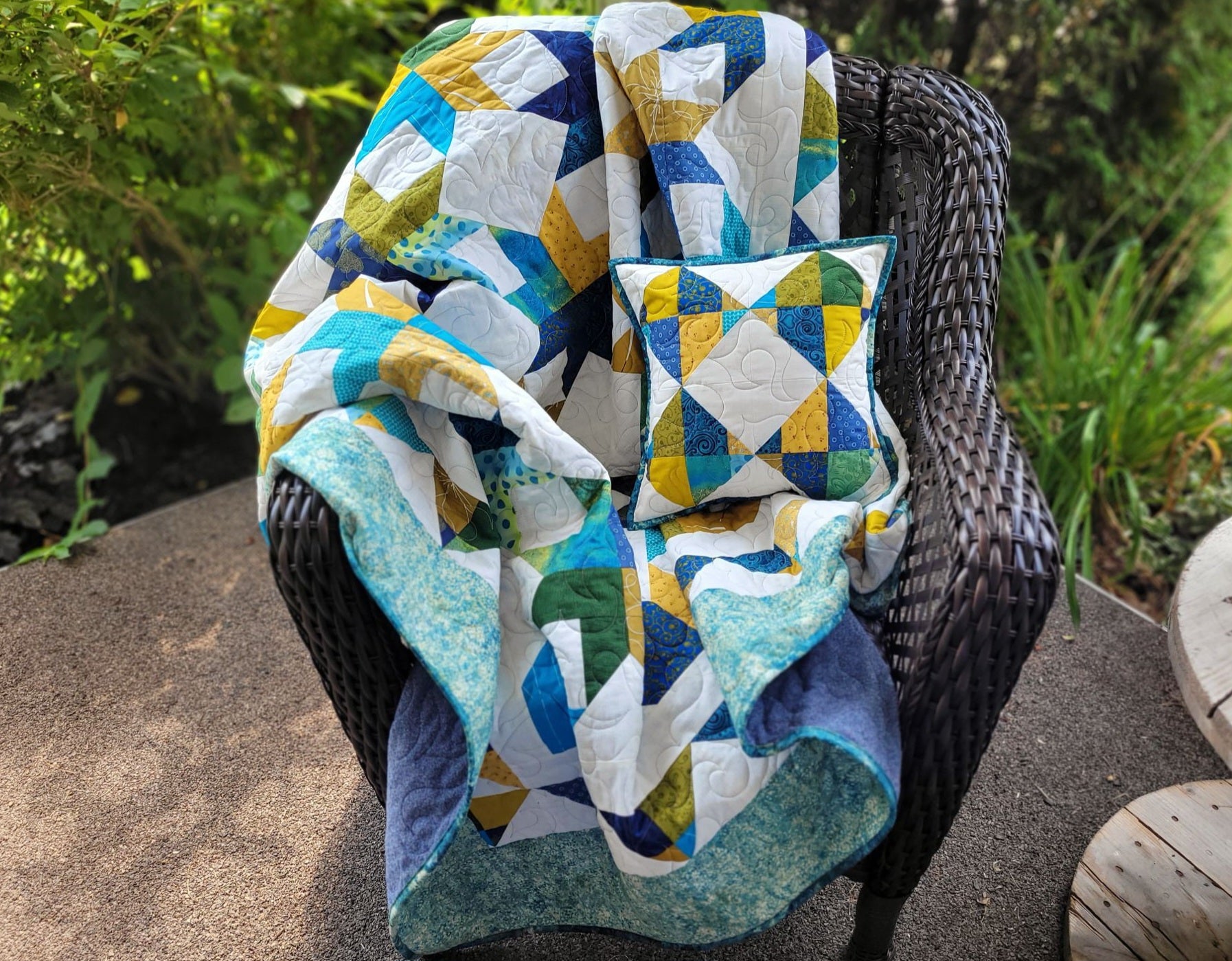 Throw quilt and matching pillow shown outdoors on a brown wicker chair.