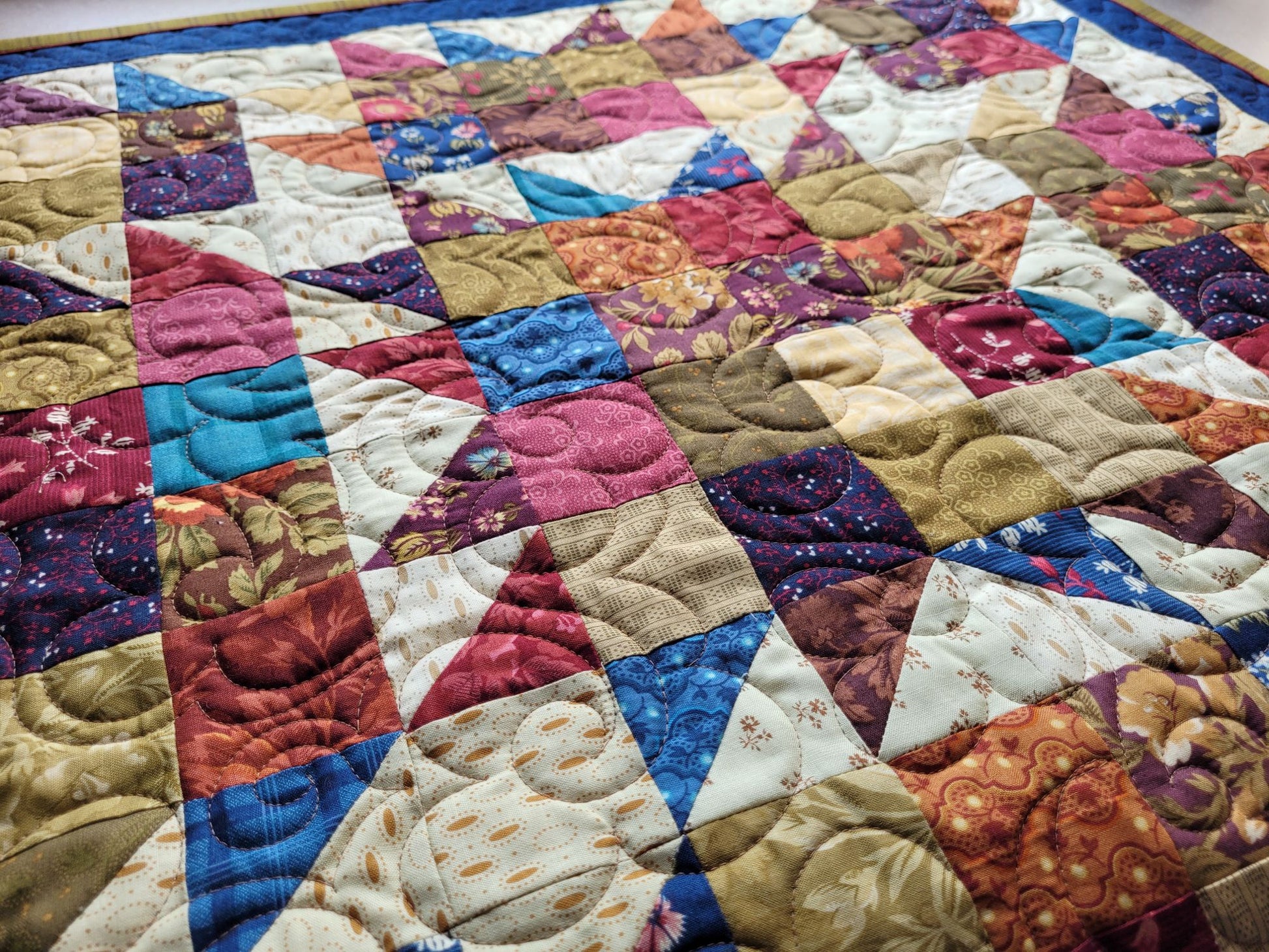 Colourful quilt with a patchwork design shown on an angled view.