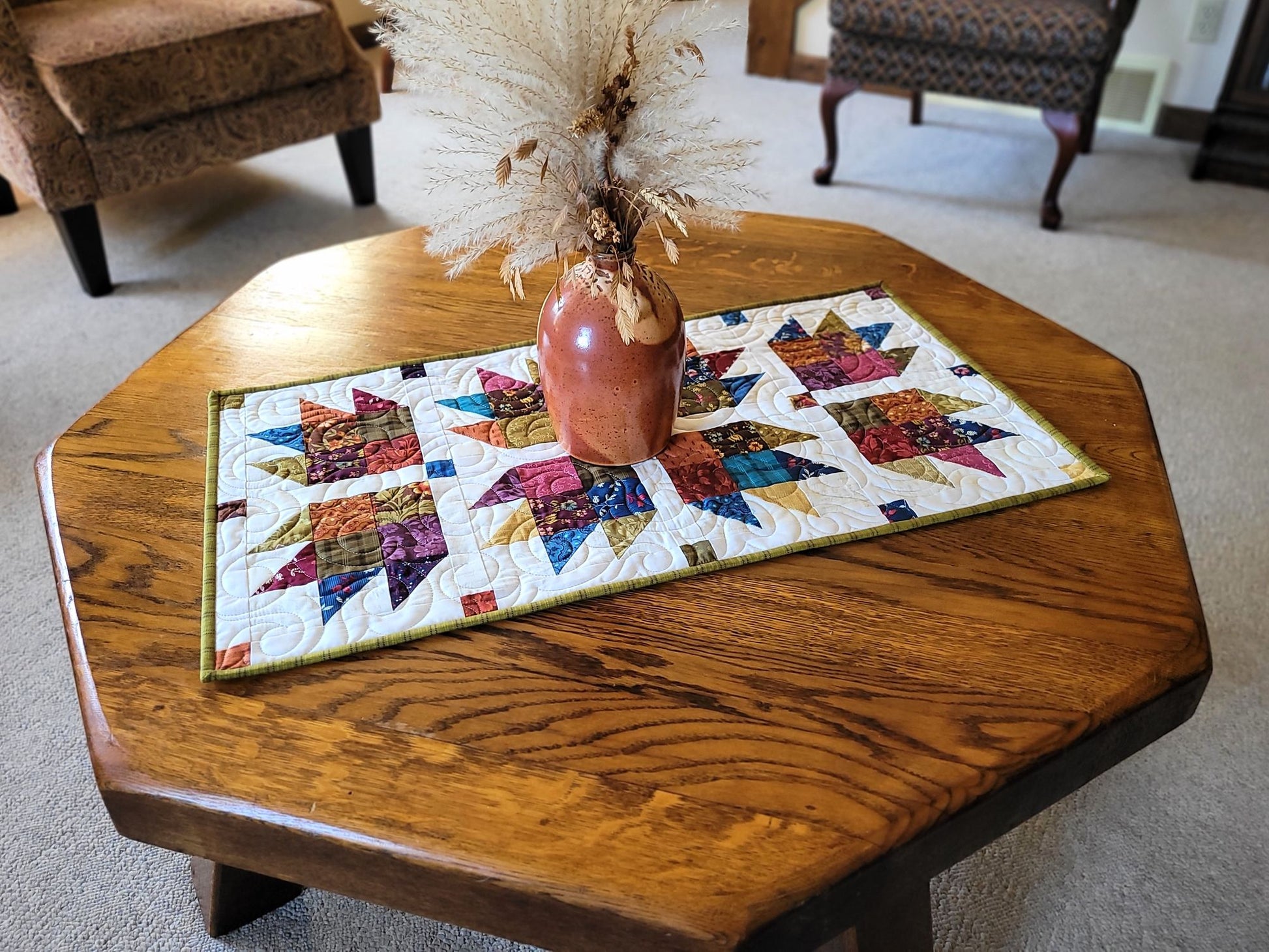 Decorative table runner with a colourful pattern on a wooden table with blurred living room furniture on the background.