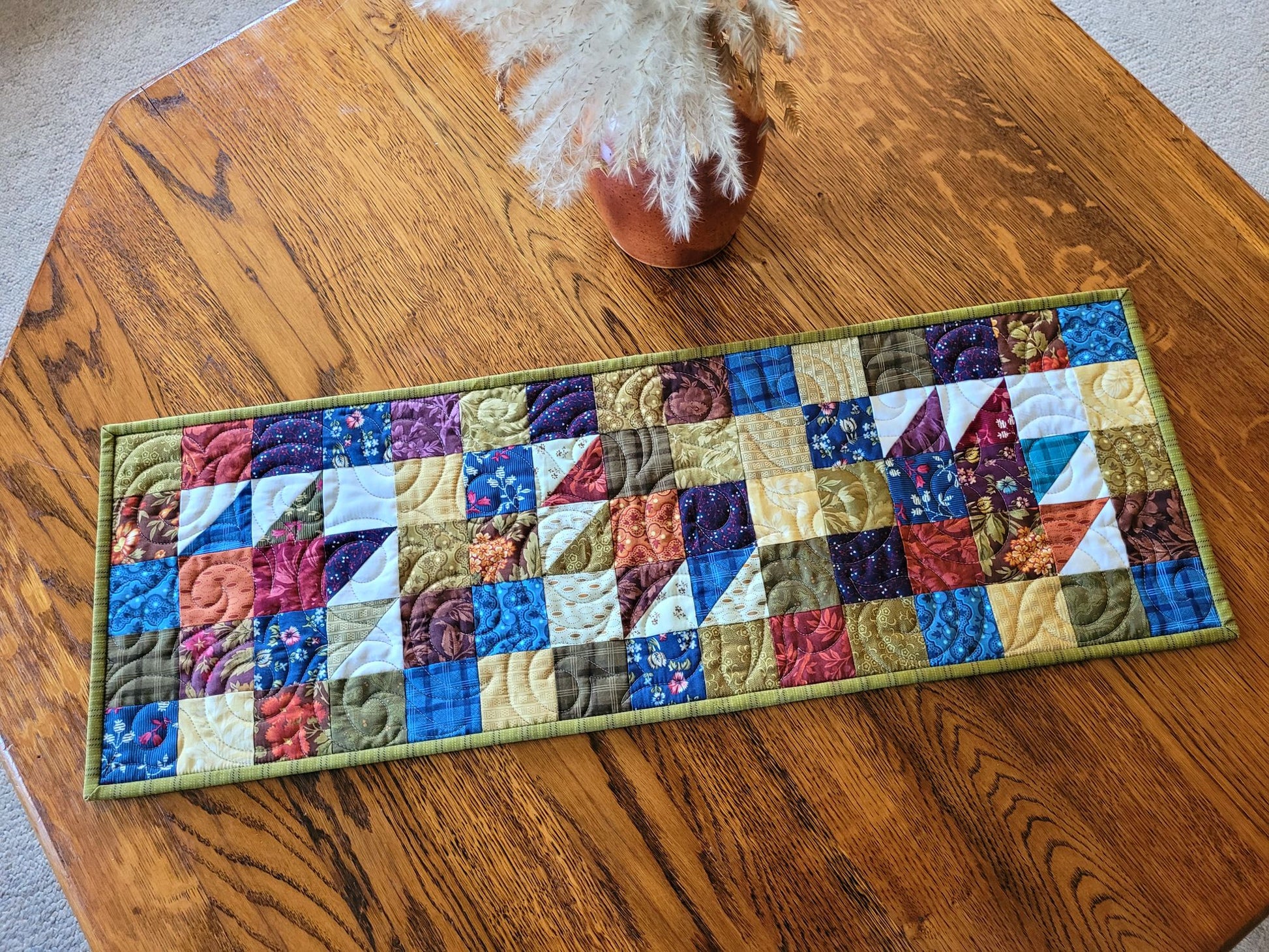 Quilted table runner with colourful patchwork design on a wooden table.