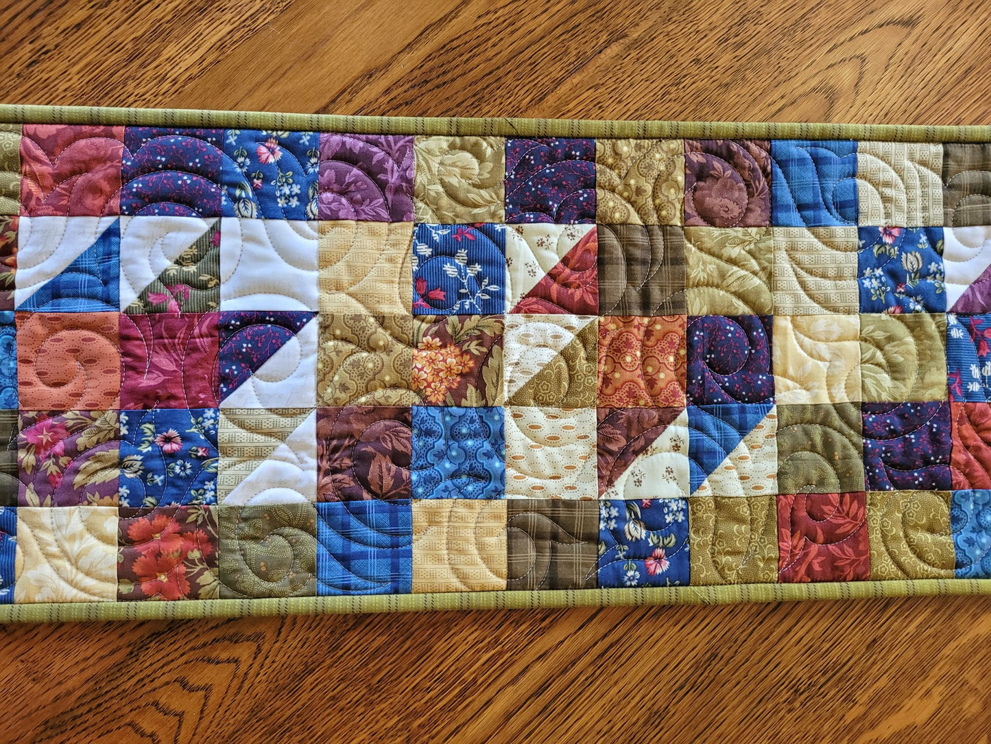 Quilted table runner with colourful patchwork design on a wooden table.