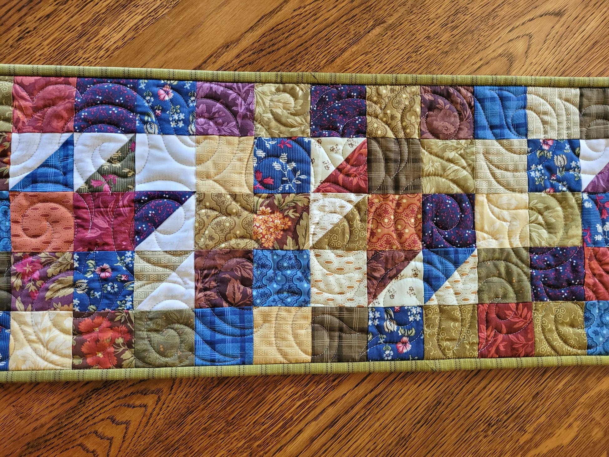 Quilted table runner with colourful patchwork design on a wooden table.