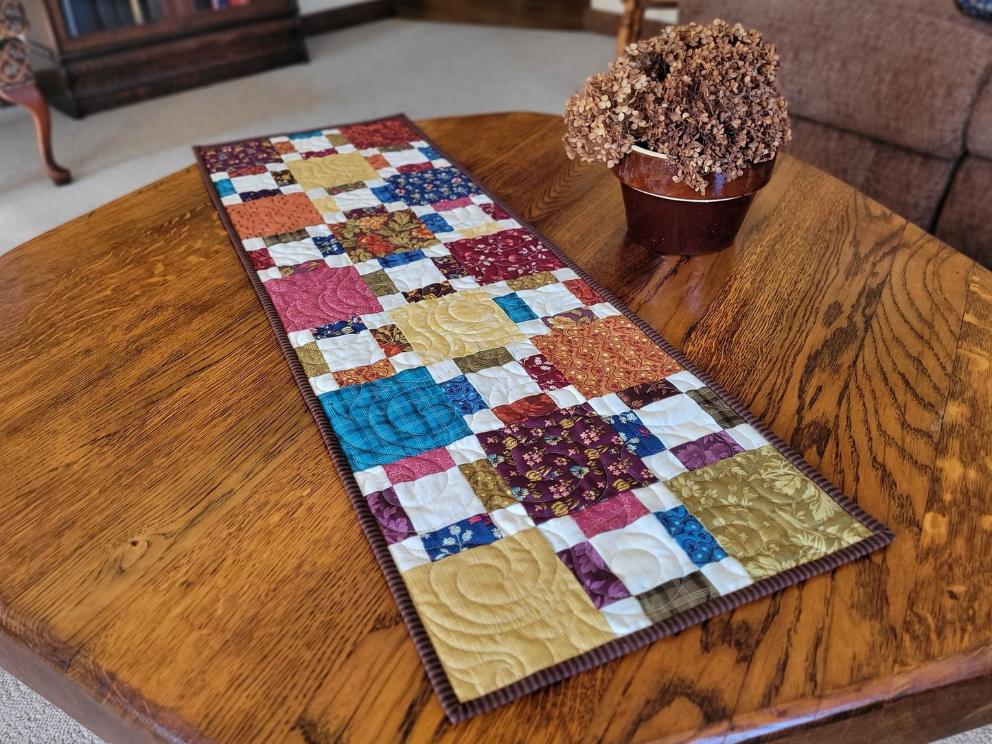 Colourful patchwork table runner on a wooden table with a plant in the background.