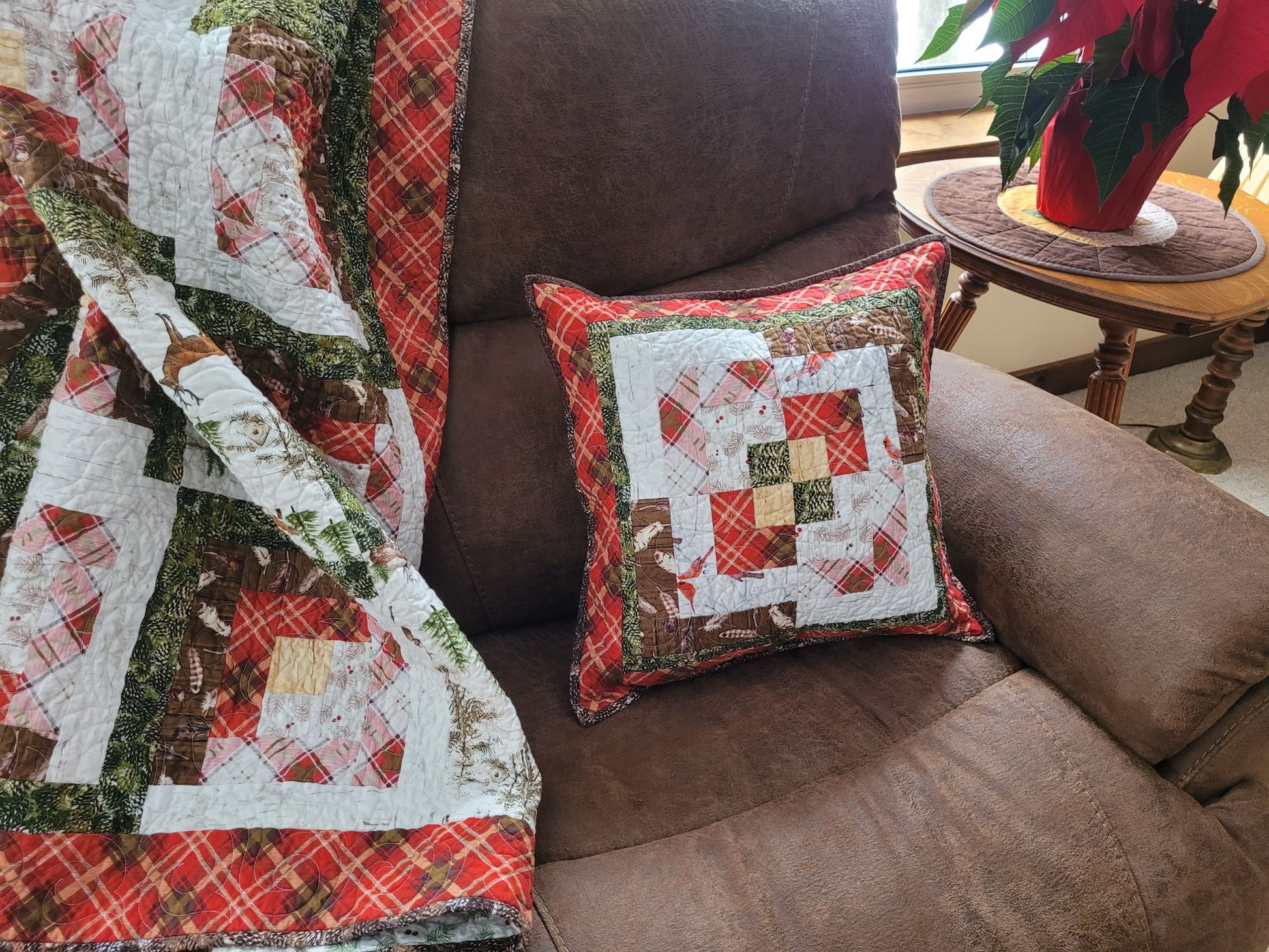 Quilted pillow and blanket on a brown sofa with a plant in the background