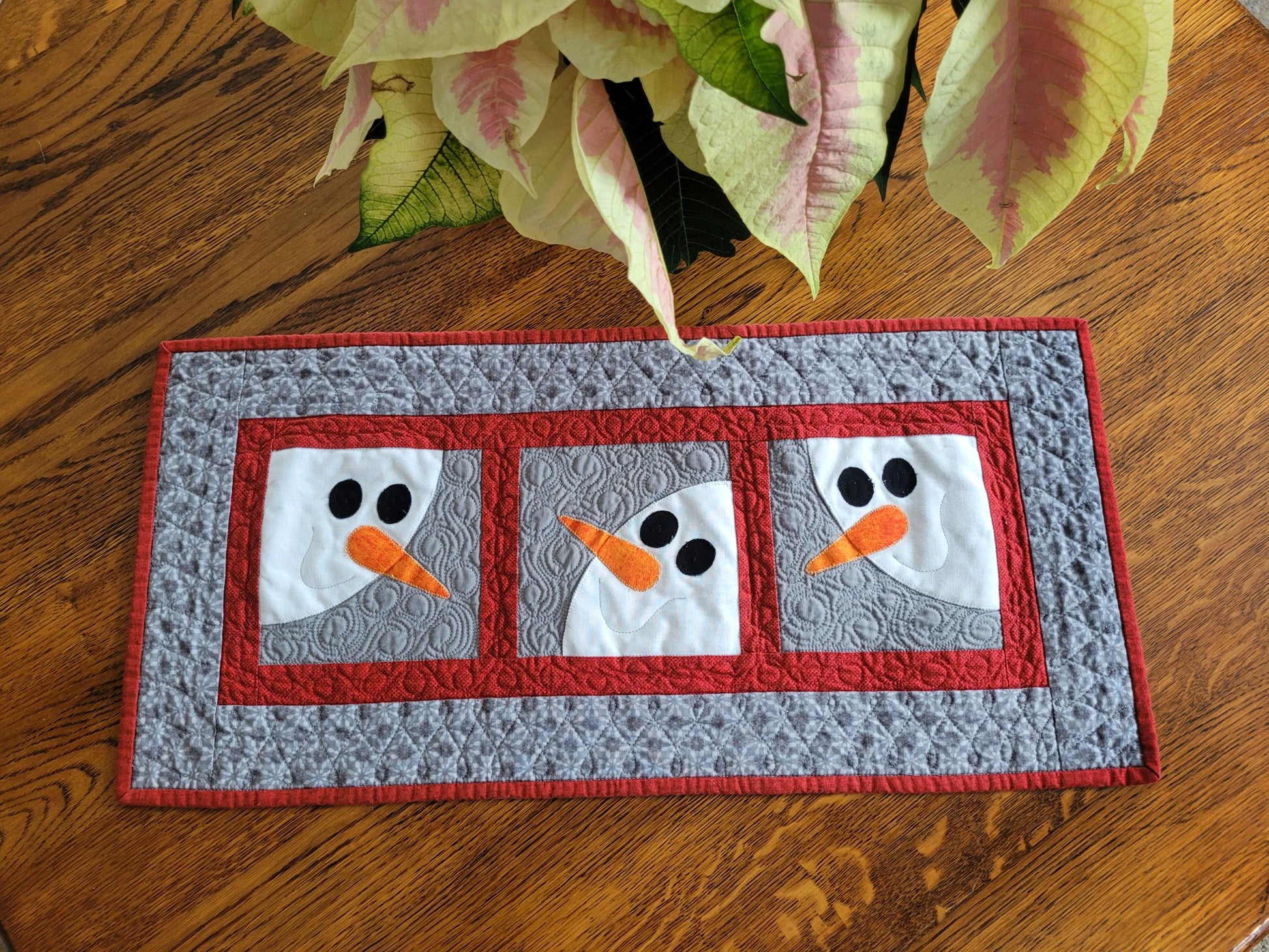 Quilted table runner with snowman design on a wooden surface