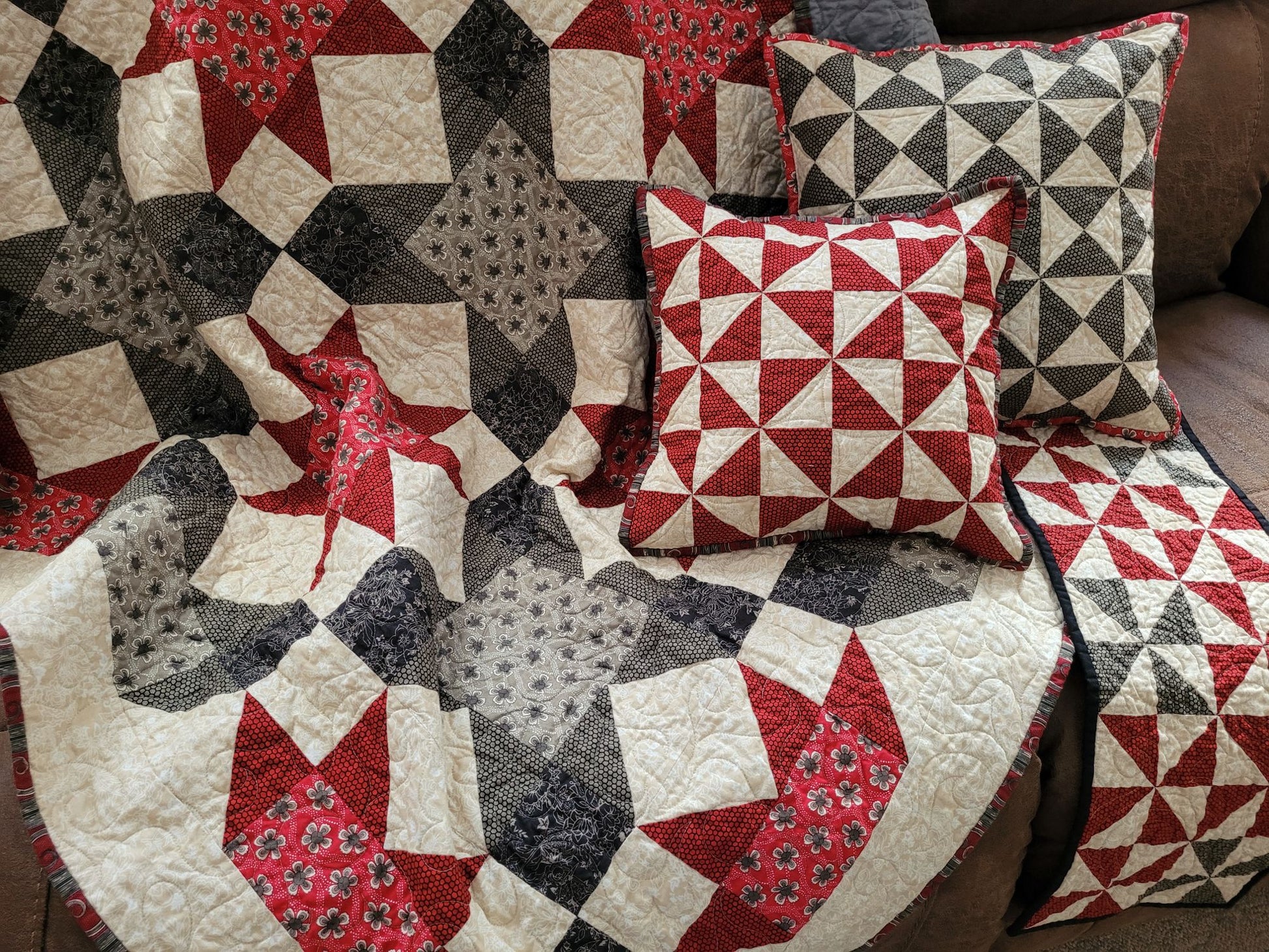 Quilt and pillows with geometric patterns in red, black, and white on a couch.