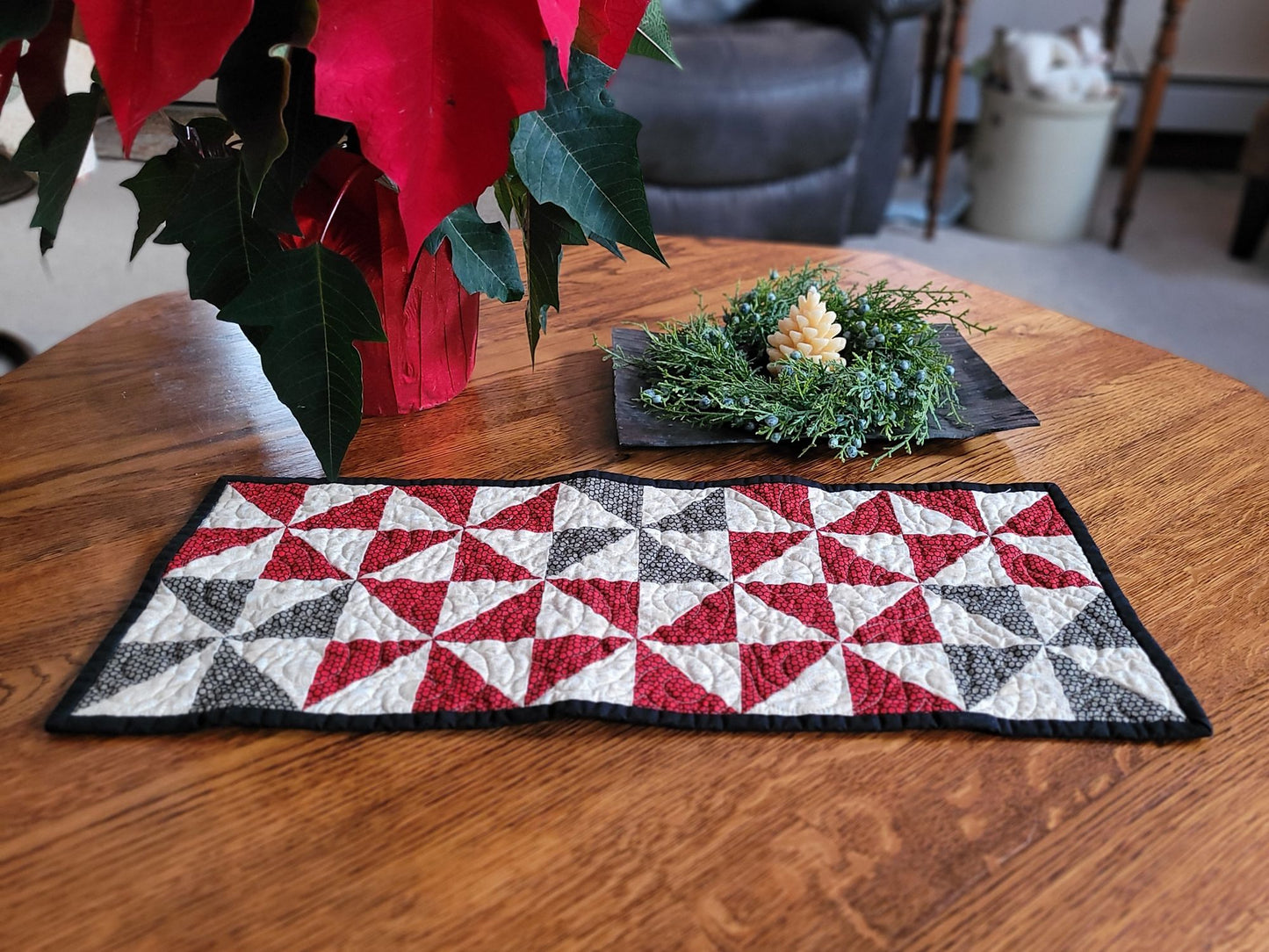 Quilted table runner with red, white, and black pattern on a wooden table with poinsettias in the background.