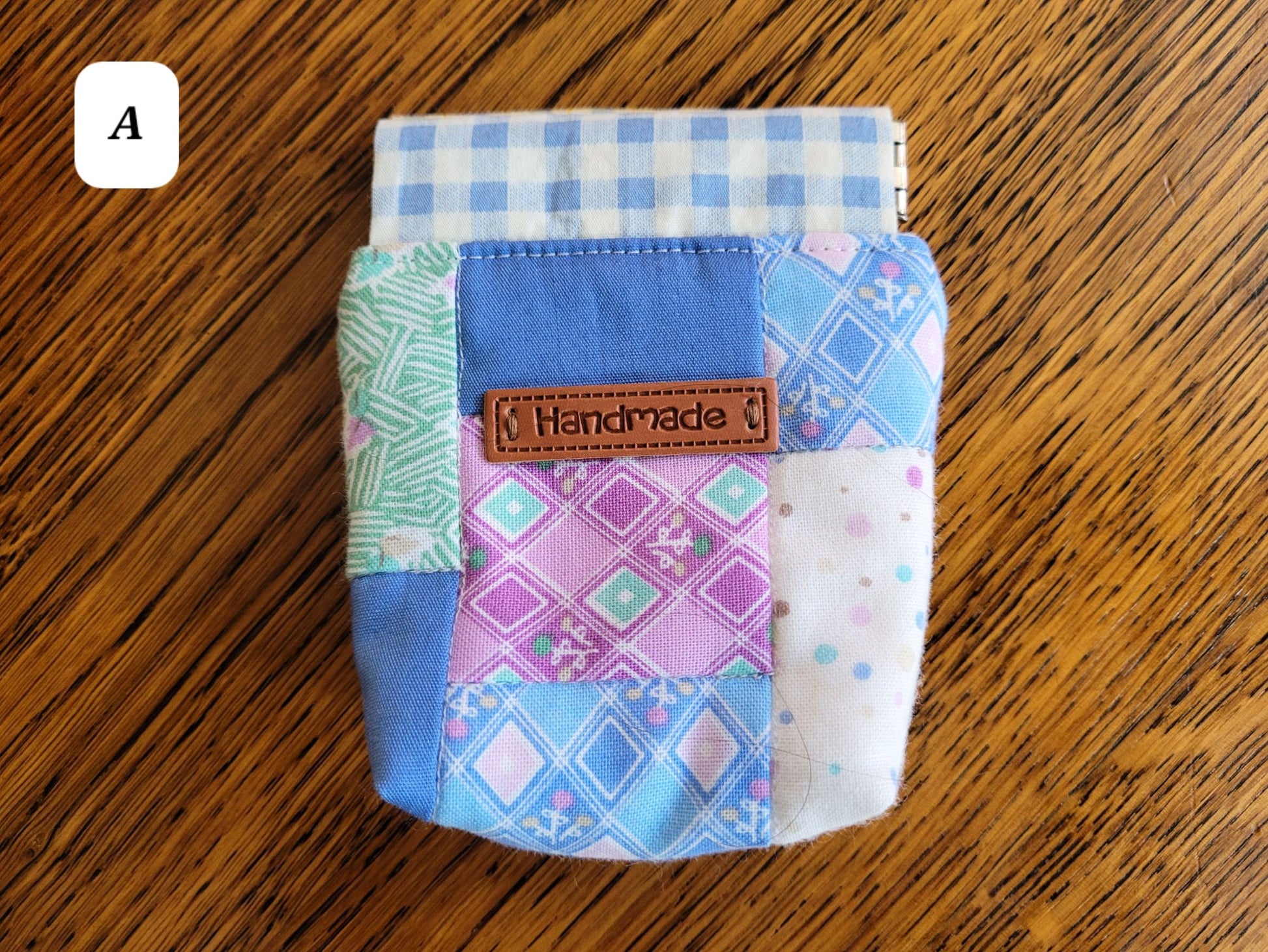 Colourful patchwork fabric pouch A with a 'Handmade' label on a wooden surface