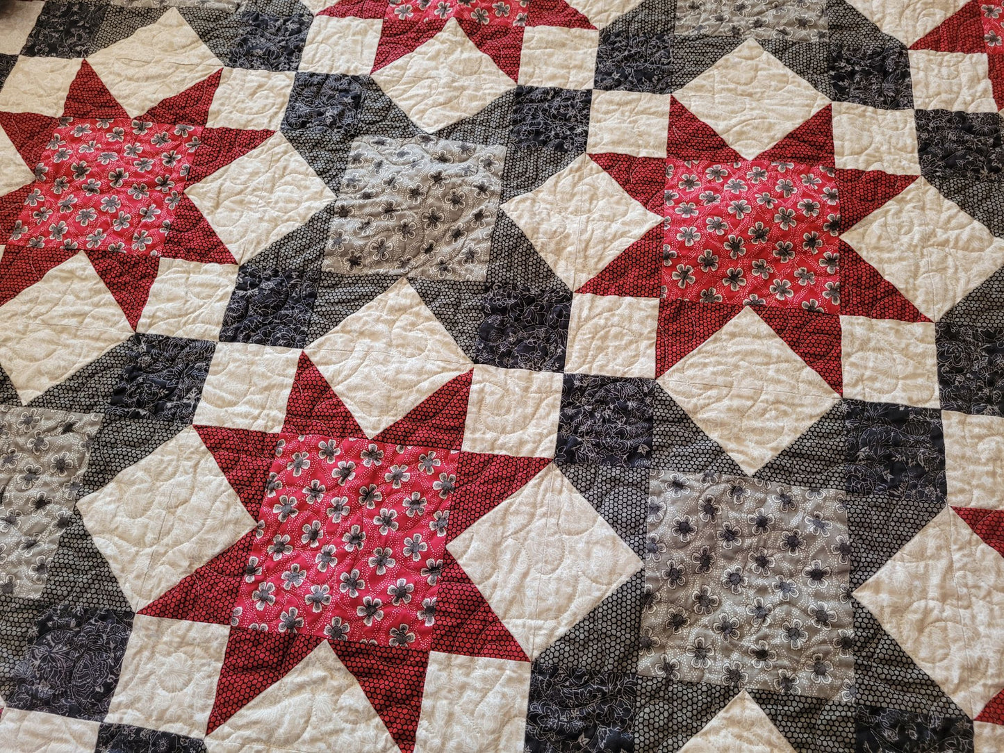 Quilt with star patterns in red, black, and gray on an ecru background.
