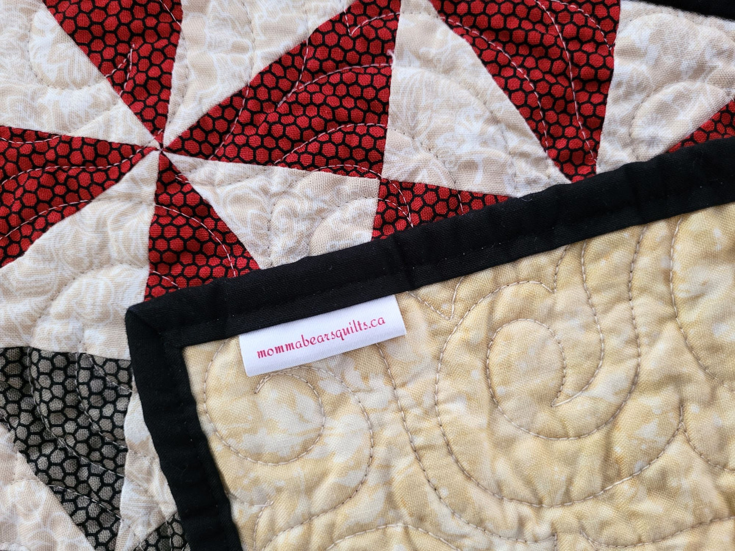 Quilt with red and black patterned triangles showing back and brand label.