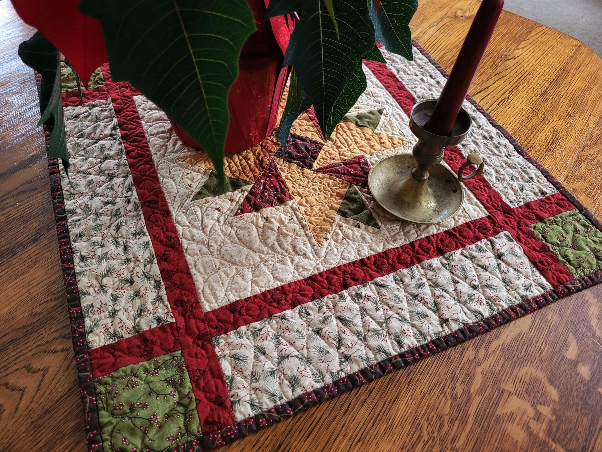 Quilted table runner with a star design on a wooden surface with a candle and poinsettia.